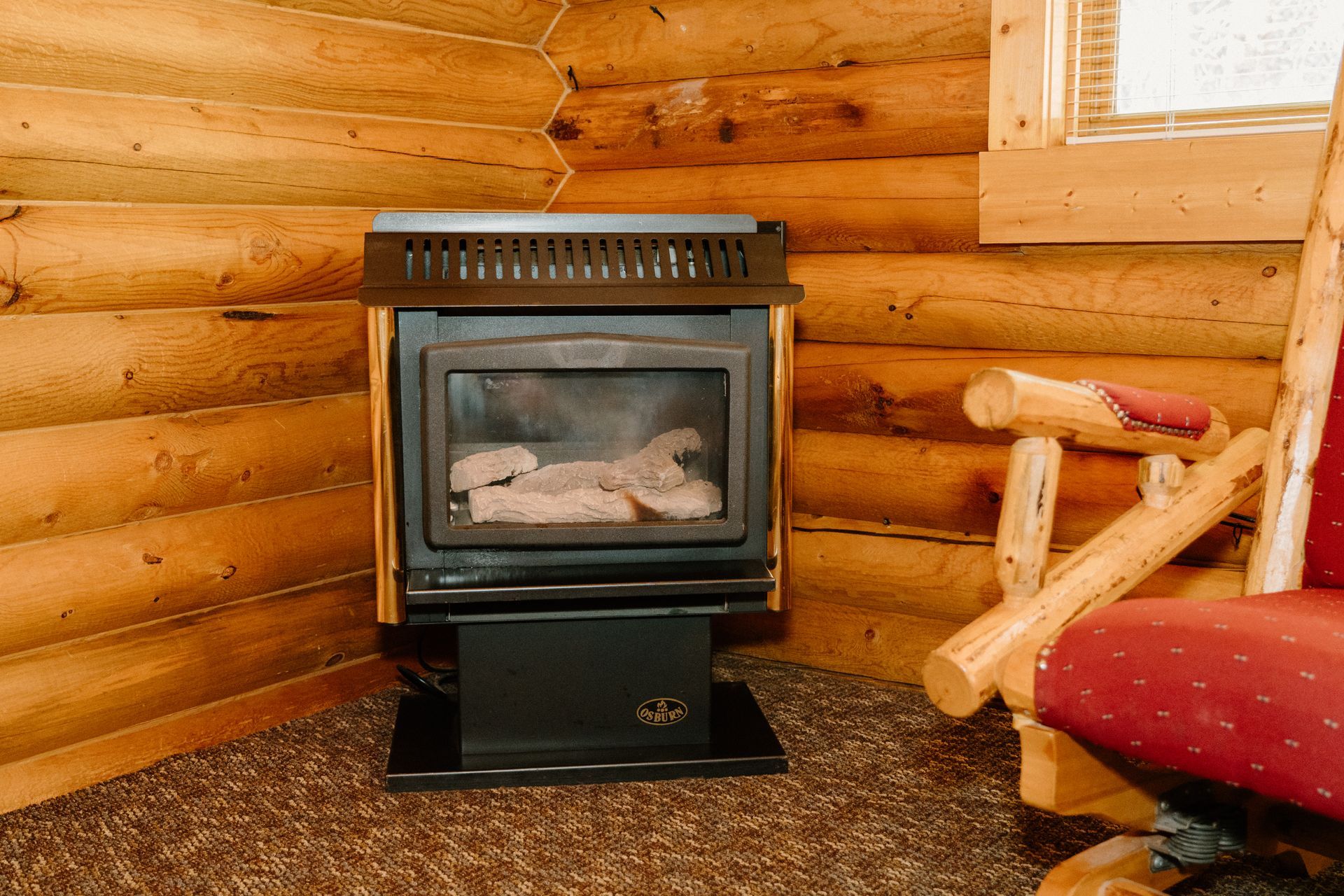 A wood stove is sitting in the corner of a log cabin next to a chair.