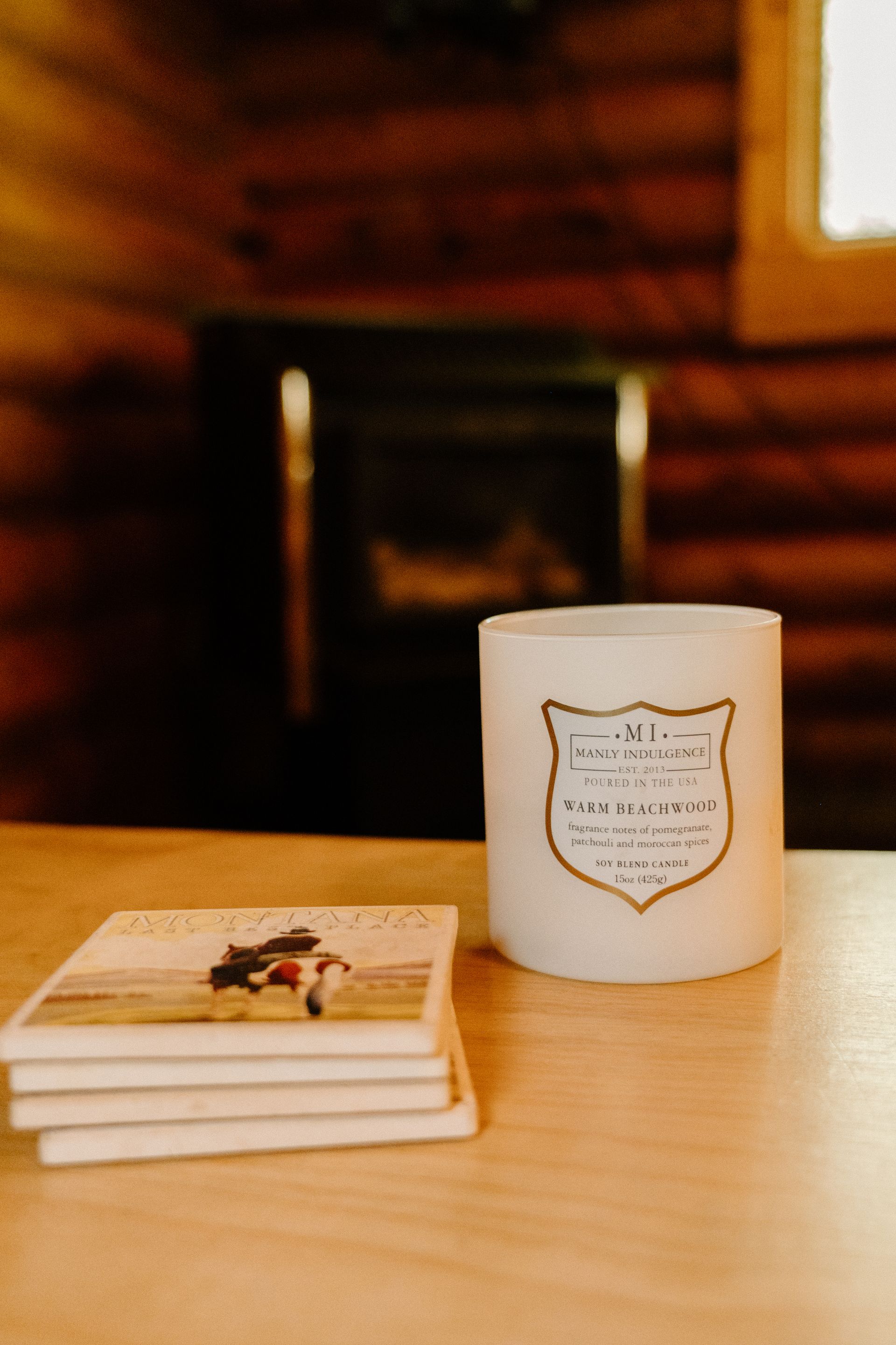 A white candle is sitting on a wooden table next to a stack of coasters.