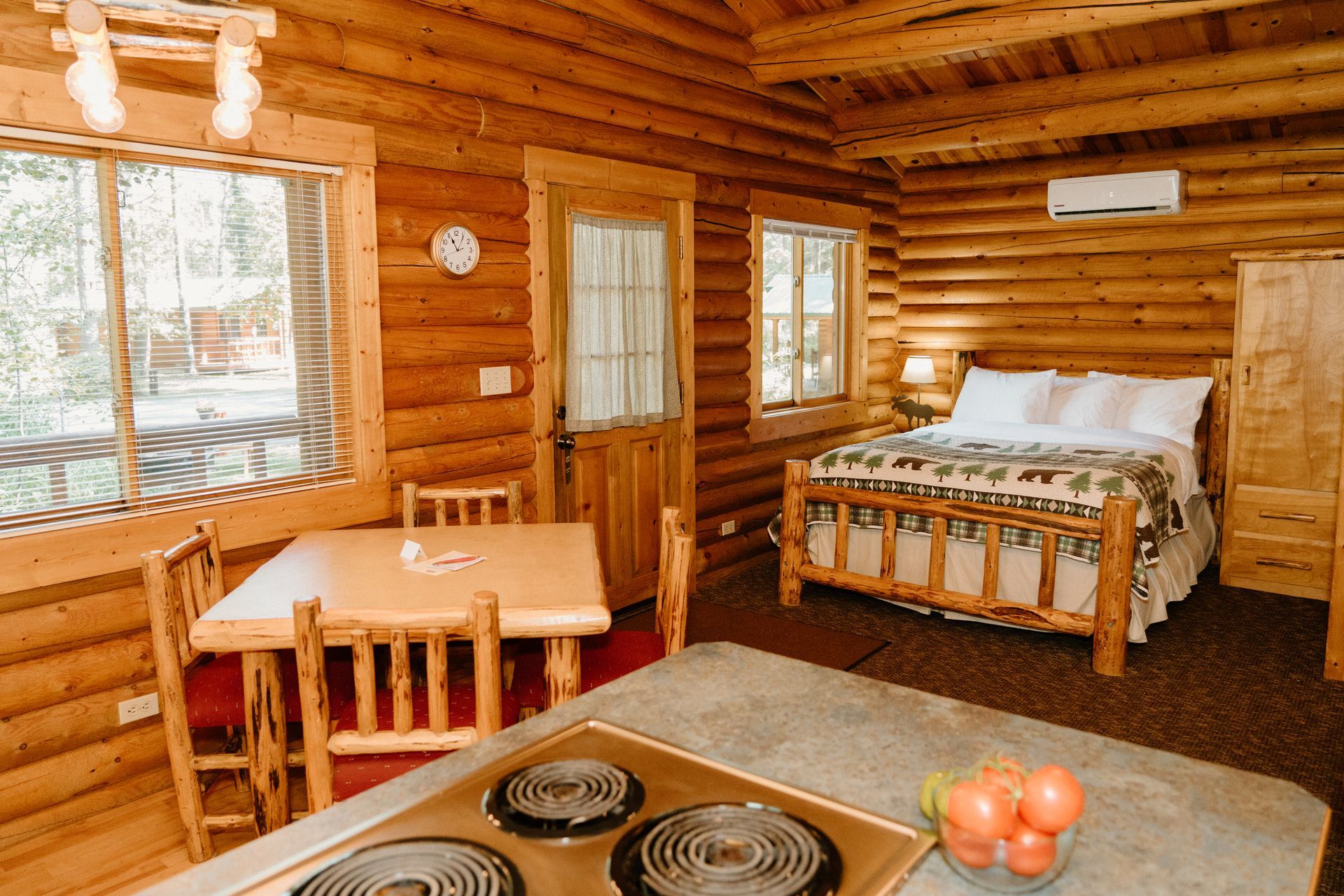 A log cabin with a bed , table , chairs and stove.