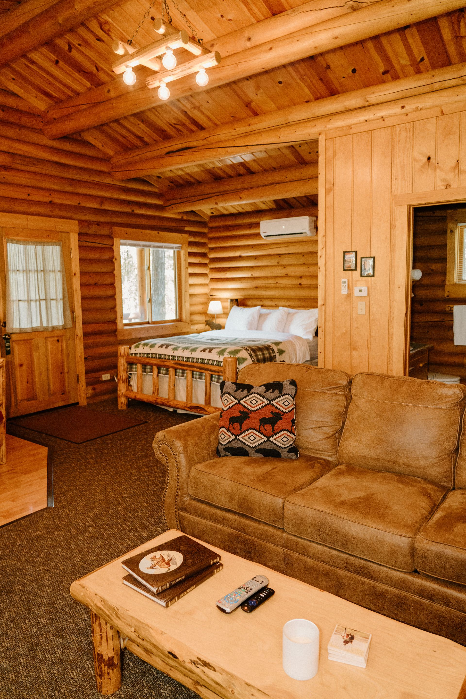 A living room in a log cabin with a couch , table , and bed.