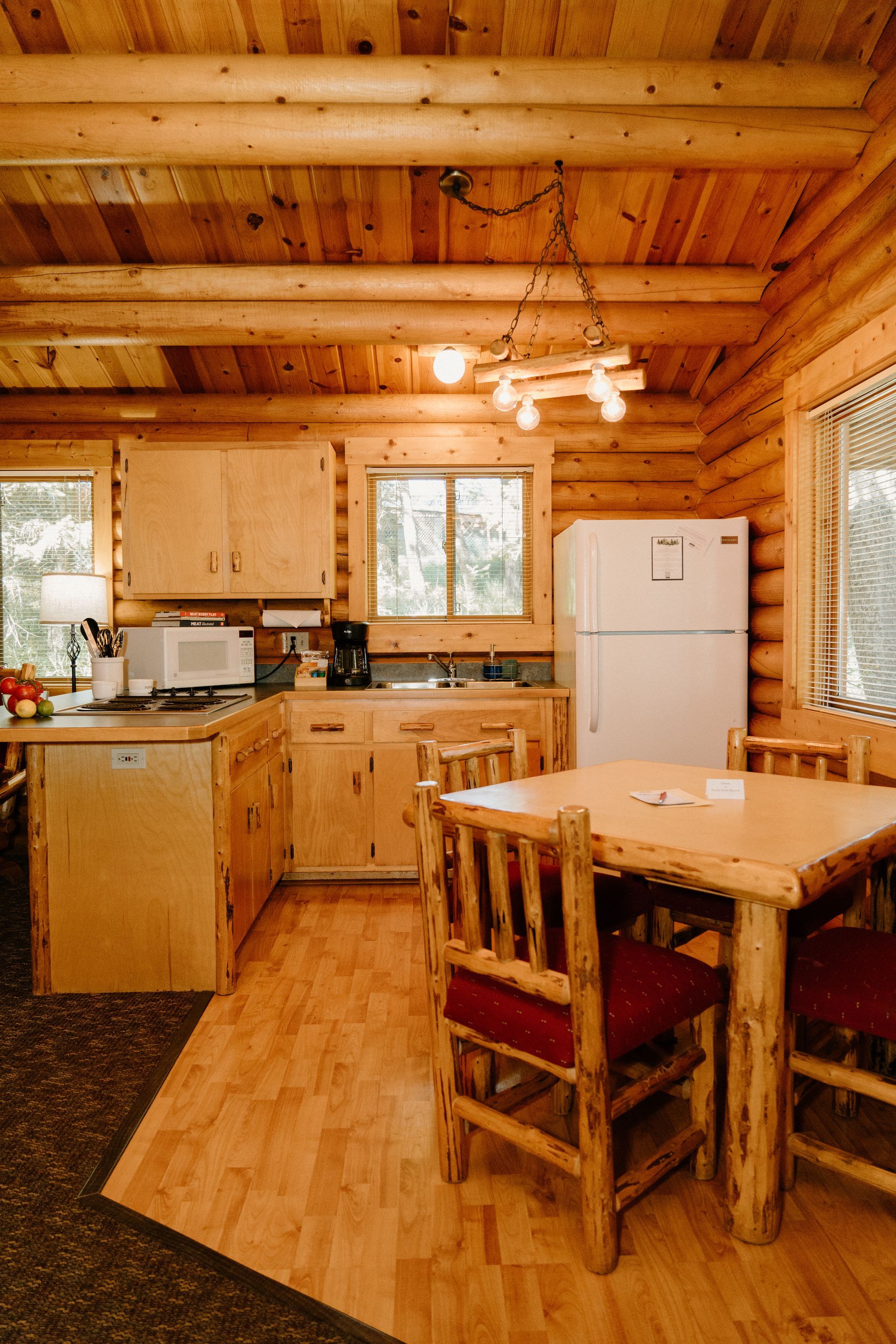 A kitchen in a log cabin with a table and chairs and a refrigerator.