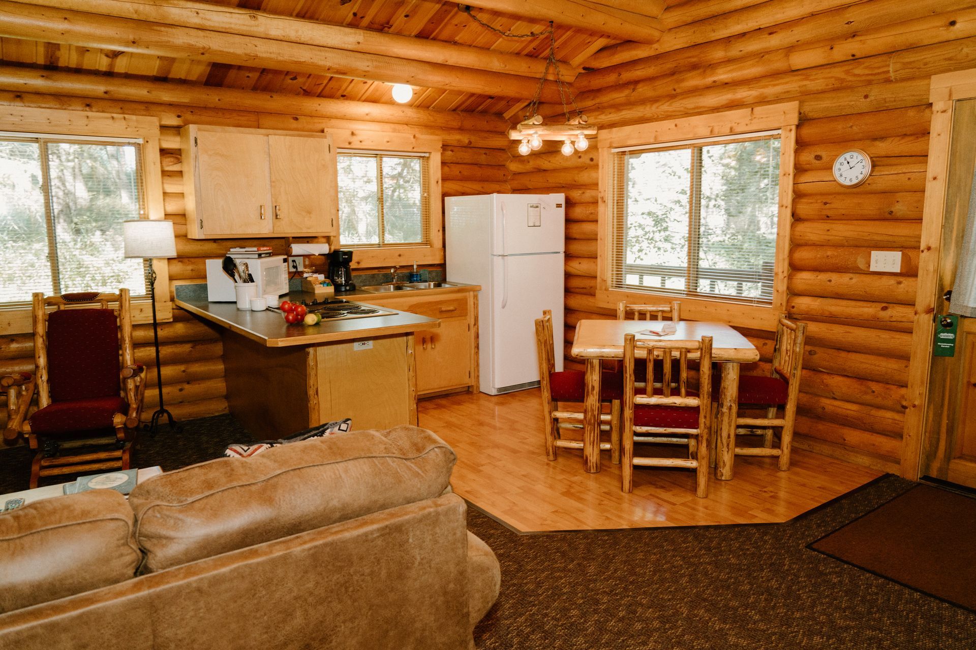 A log cabin with a living room , dining room , kitchen and refrigerator.