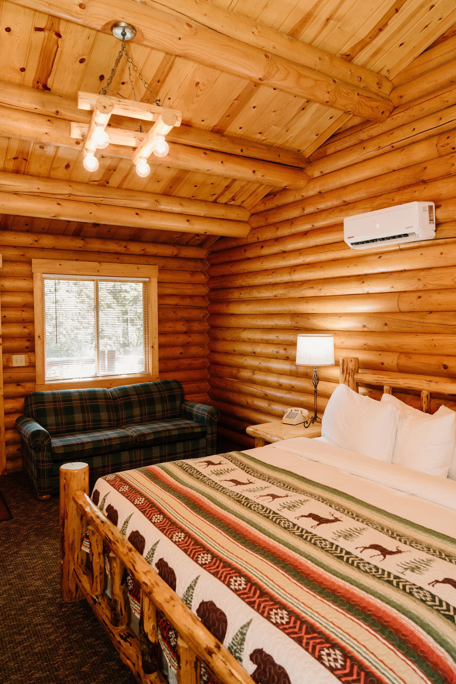 A bedroom in a log cabin with a bed , couch , and window.