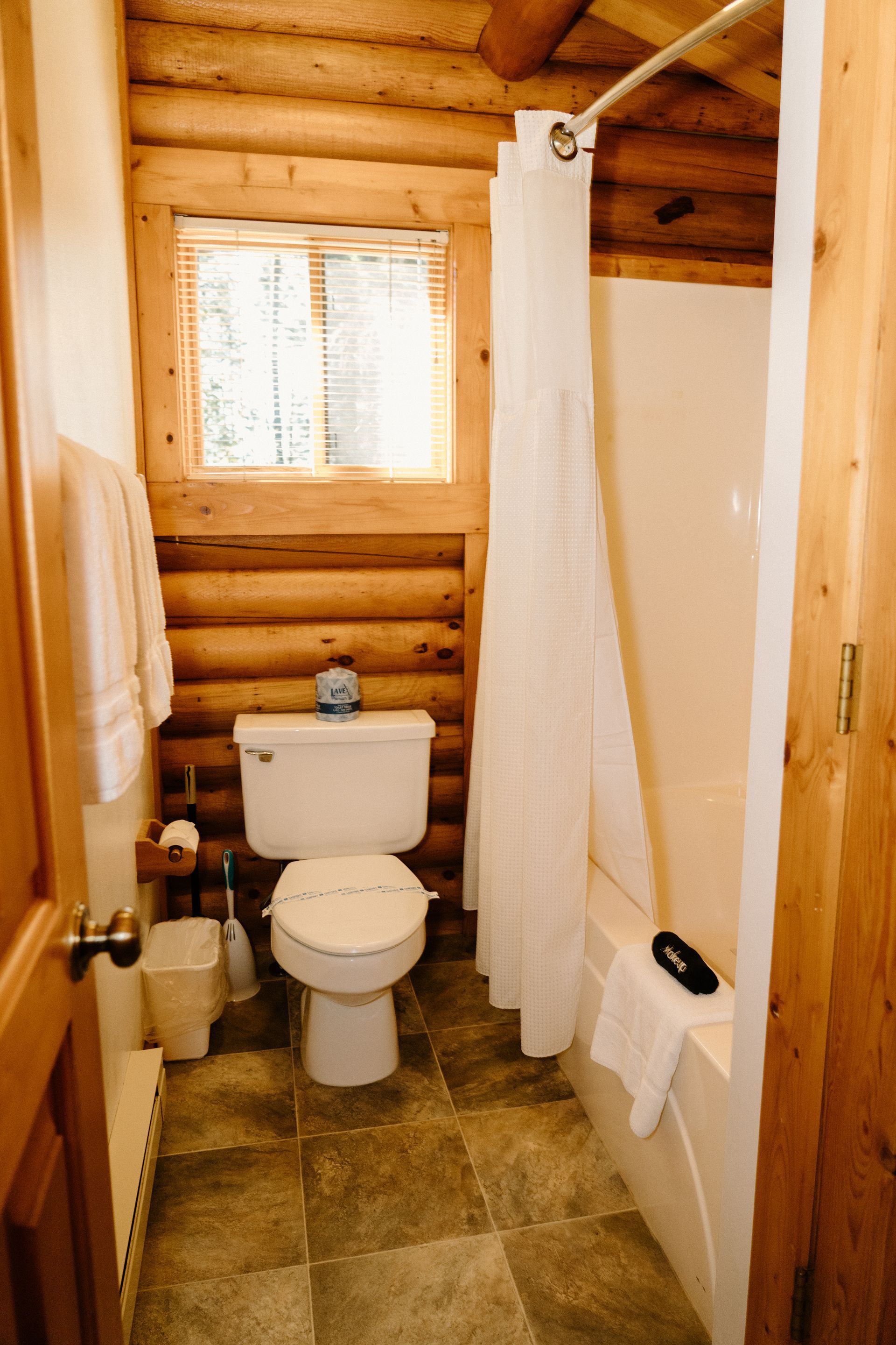 A bathroom in a log cabin with a toilet , shower and tub.