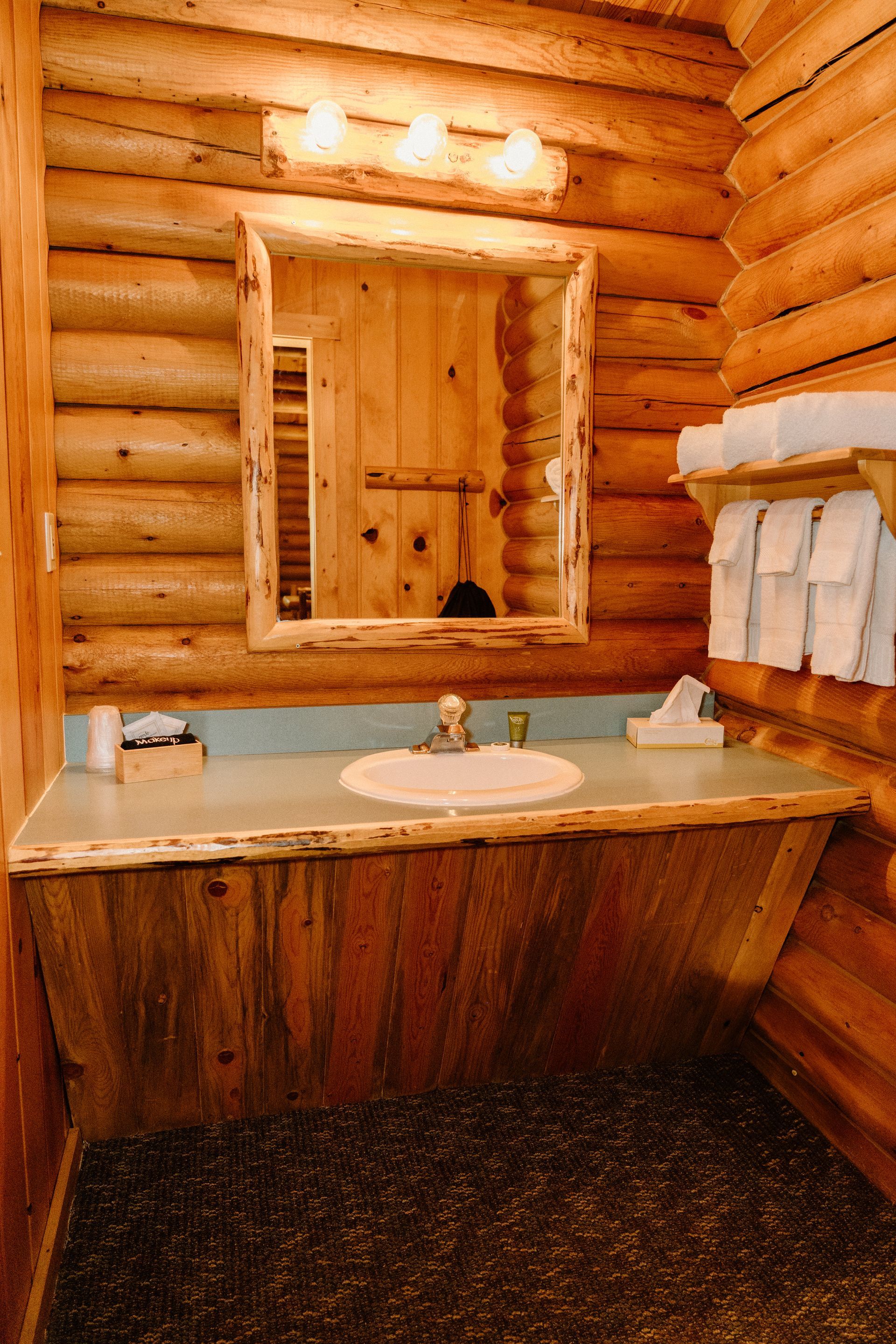 A bathroom in a log cabin with a sink , mirror and towels.