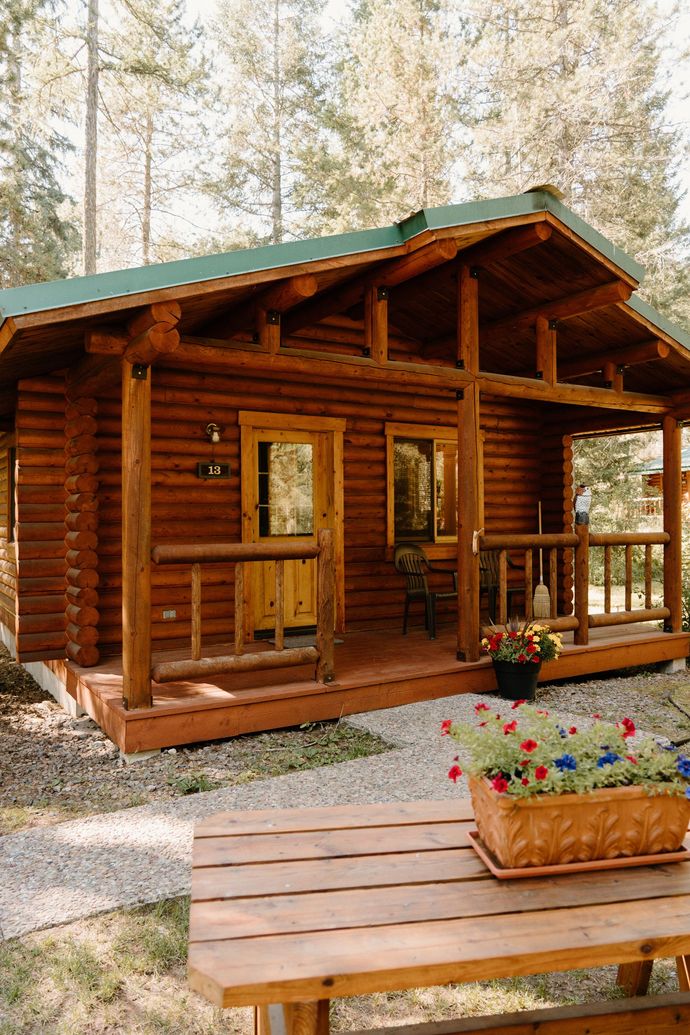 A small log cabin with a porch and a picnic table in front of it.