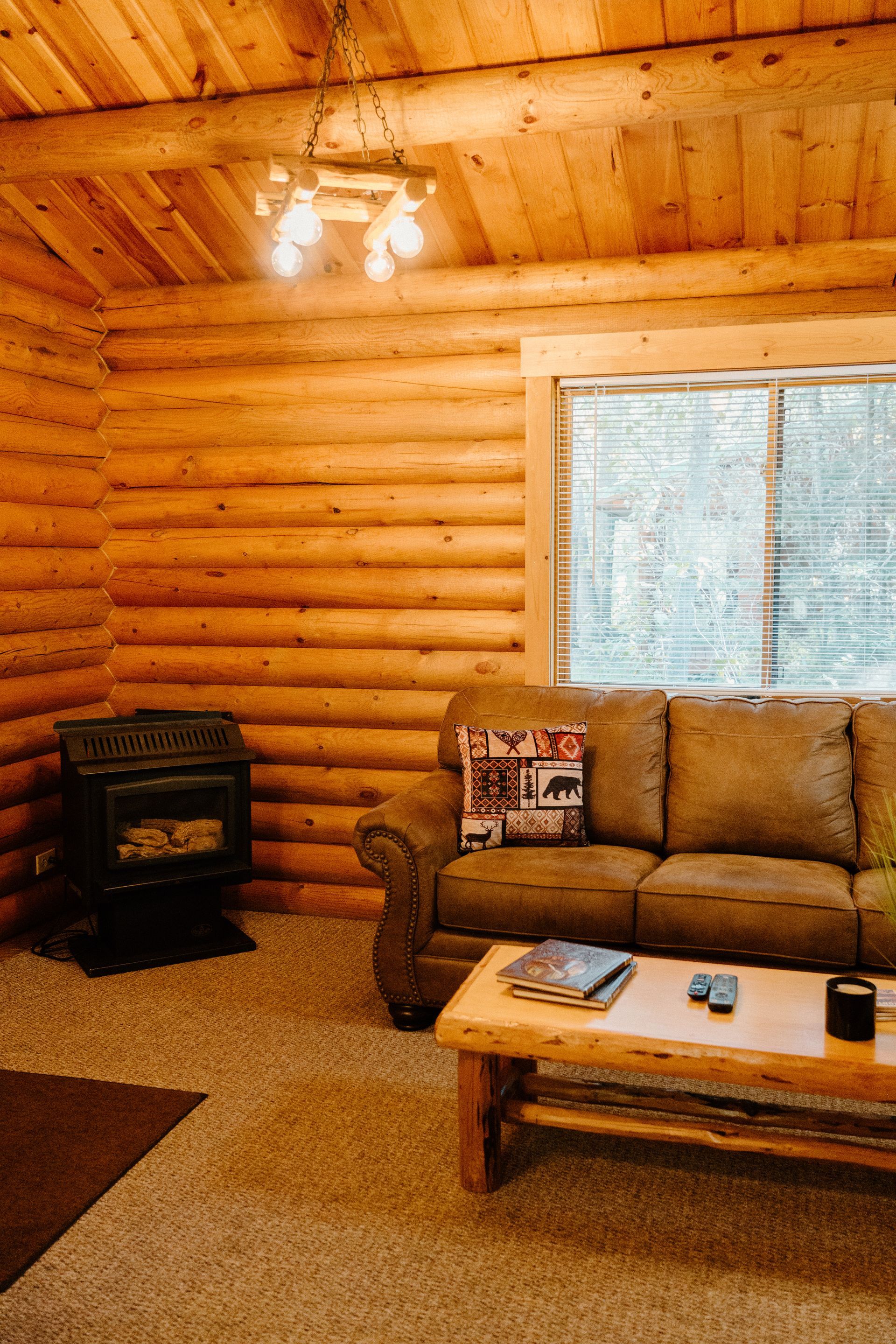 A living room in a log cabin with a couch , coffee table and fireplace.