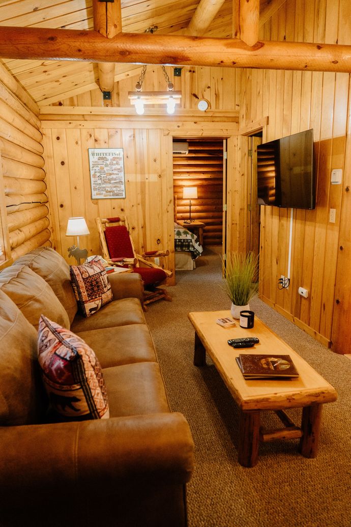 A living room in a log cabin with a couch , chair , coffee table and television.