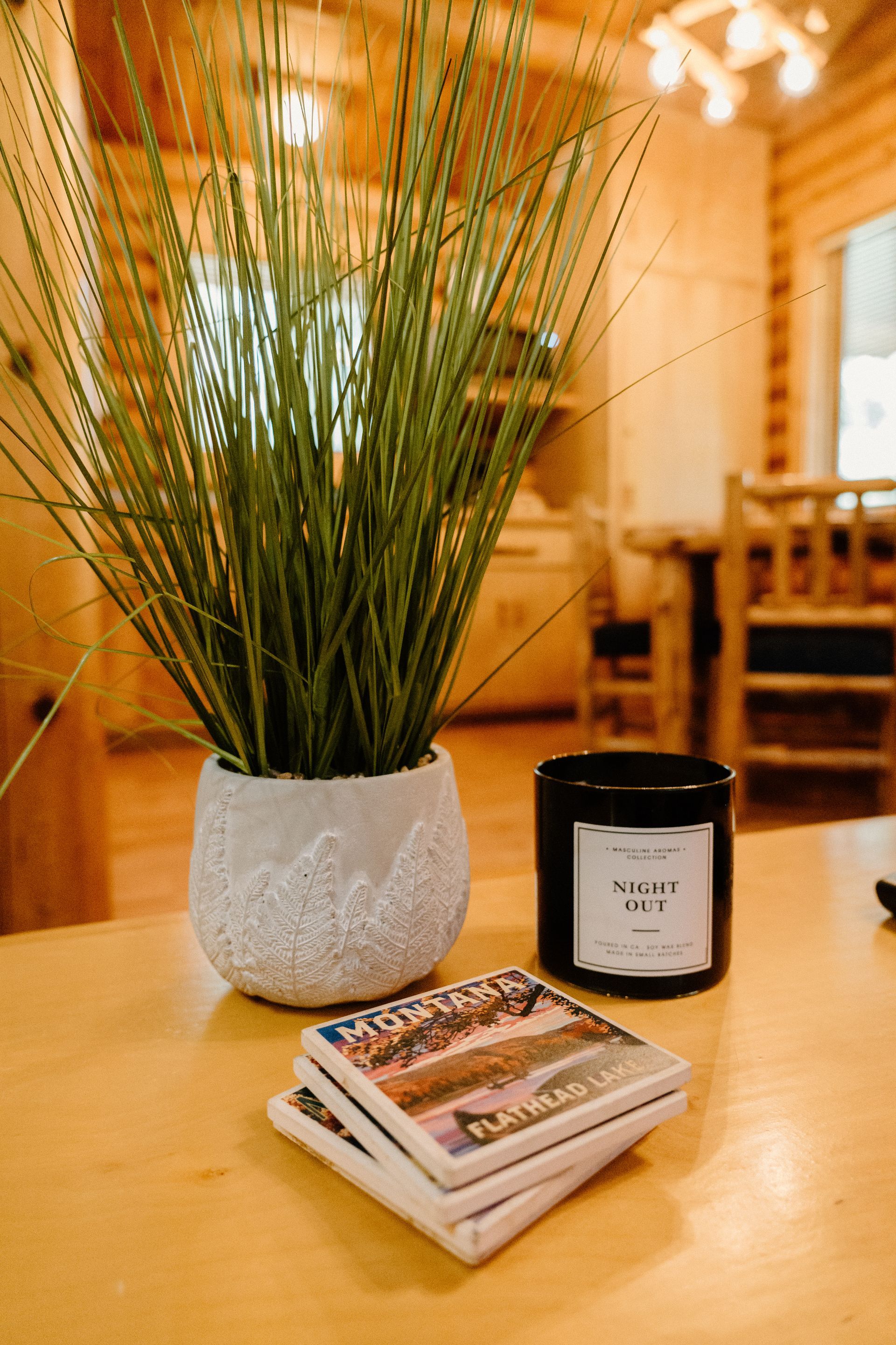 A potted plant , a candle , and coasters are on a wooden table.