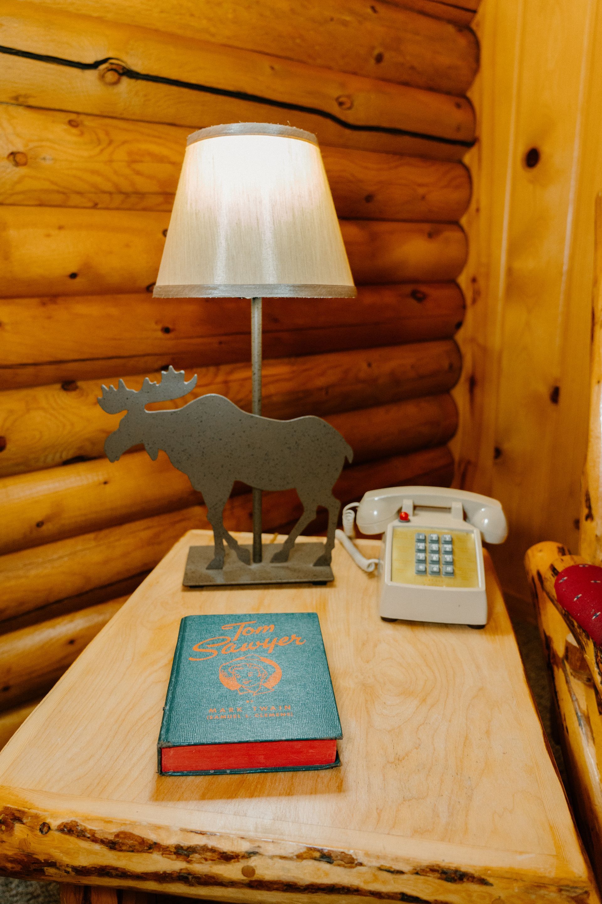 A moose lamp is on a wooden table next to a book and a phone.