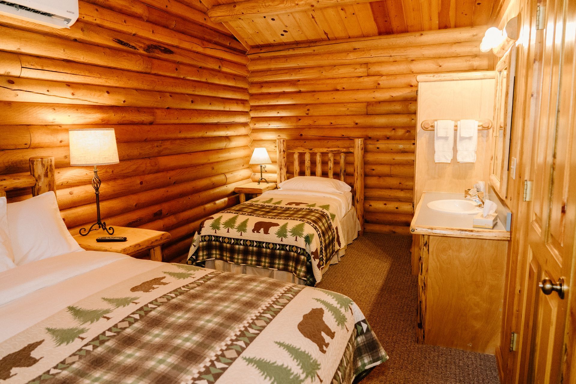 A bedroom in a log cabin with two beds and a sink.