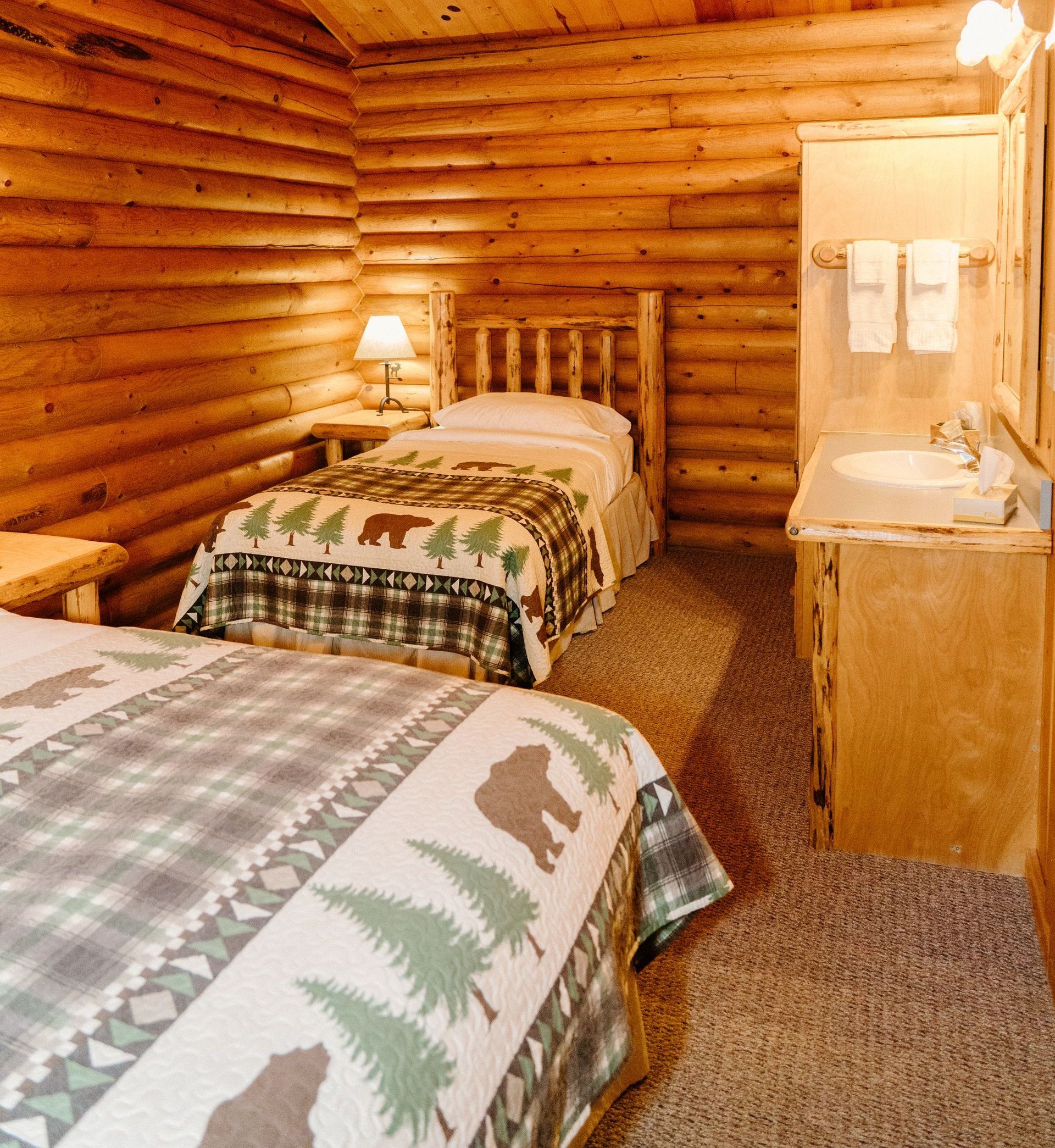 A bedroom in a log cabin with two beds and a sink.