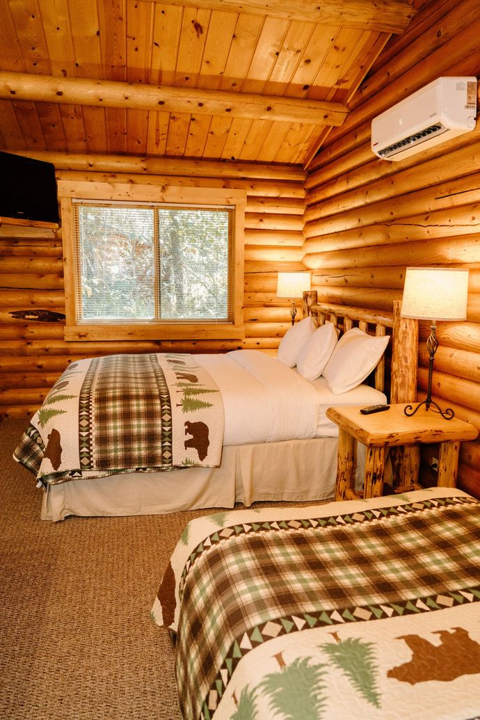 A bedroom in a log cabin with two beds and a television.