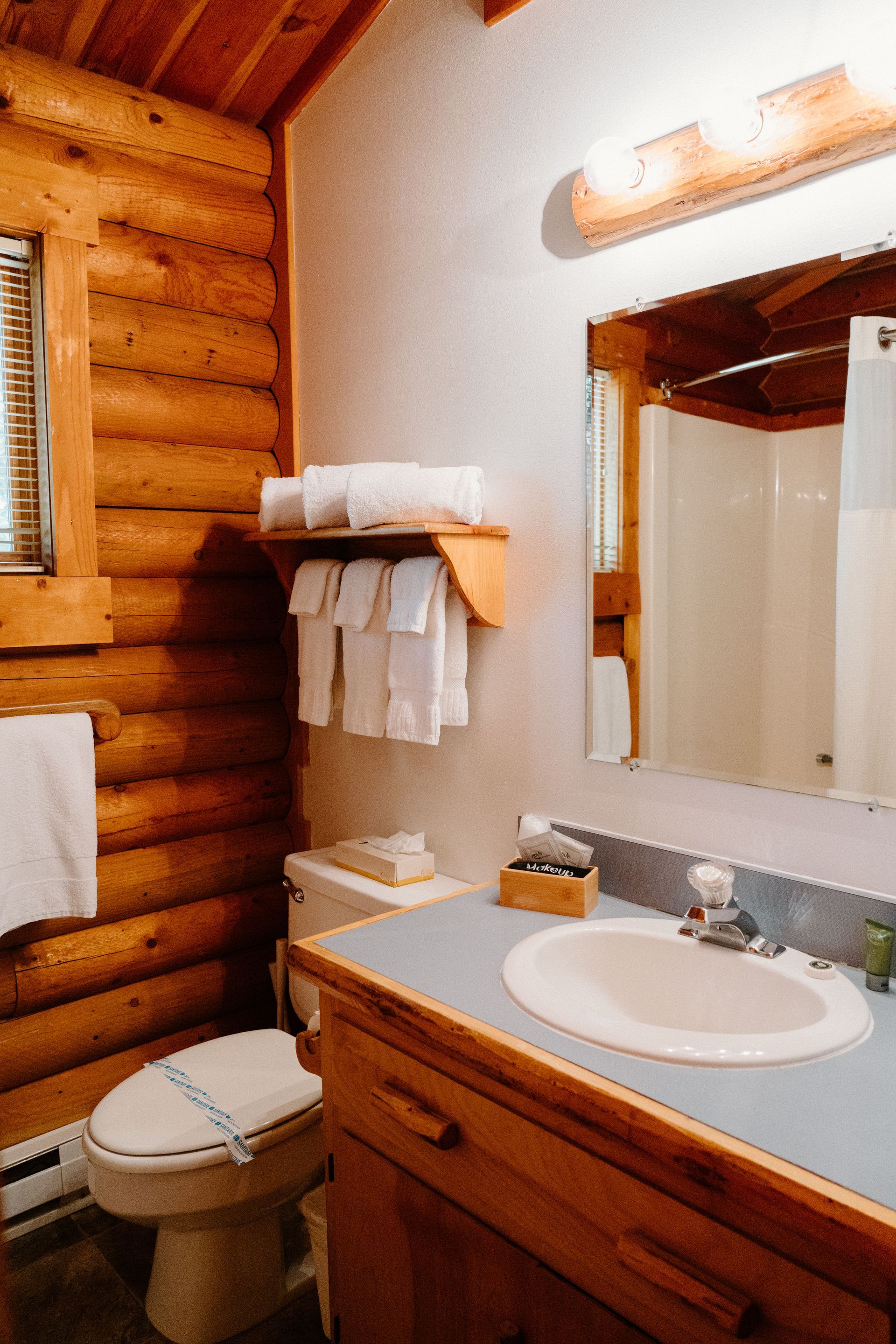 A bathroom in a log cabin with a toilet , sink and mirror.