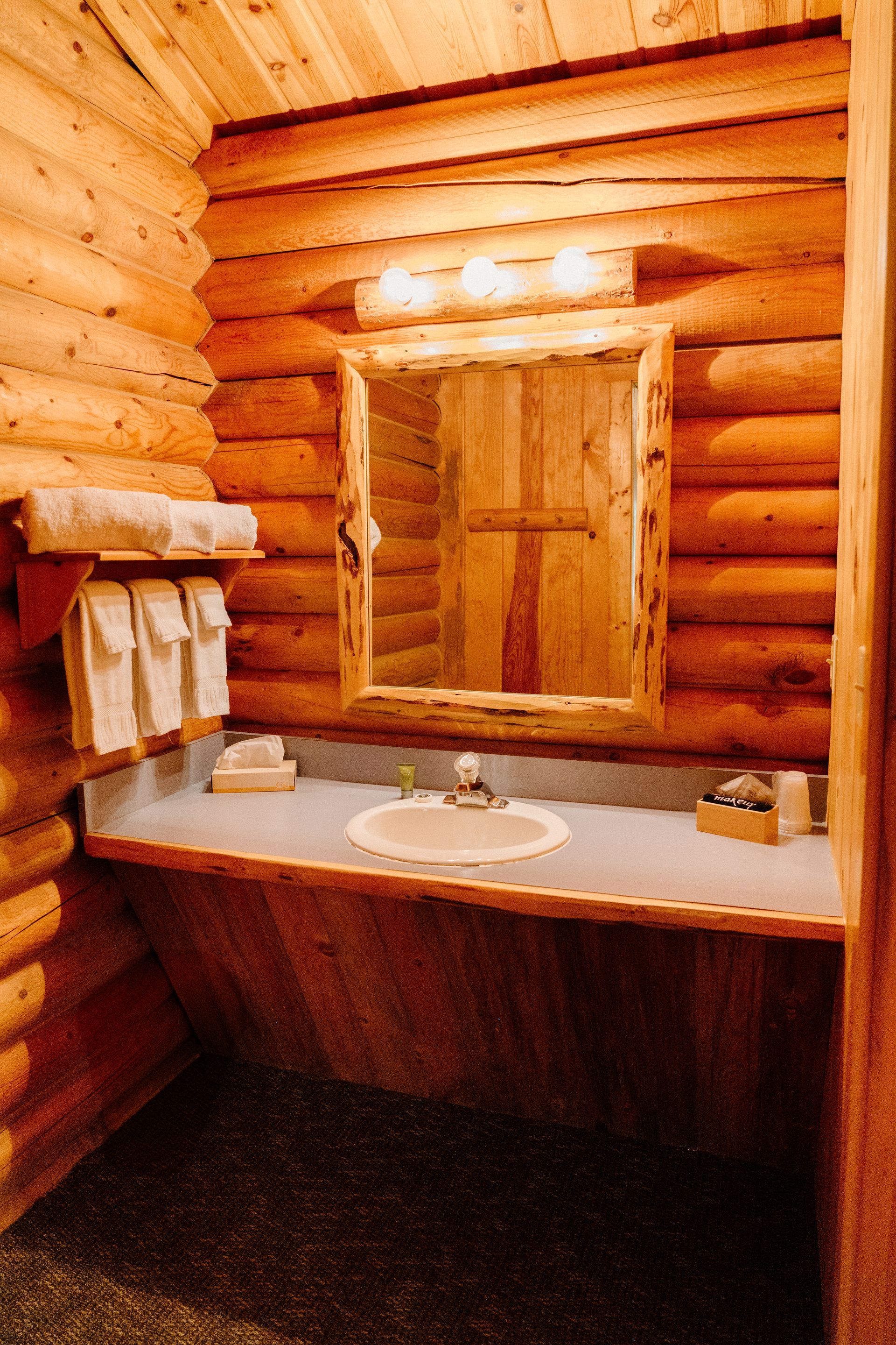 A bathroom in a log cabin with a sink , mirror and towels.