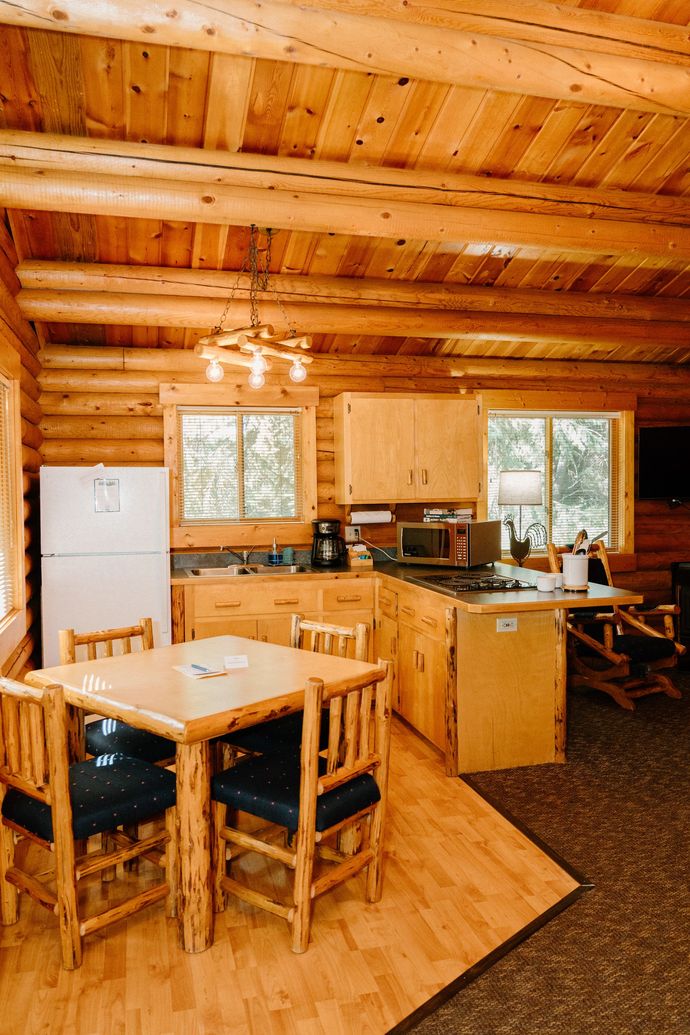 There is a table and chairs in the kitchen of a log cabin.