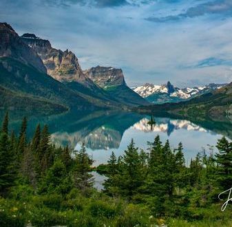 A lake surrounded by mountains and trees with mountains reflected in the water.