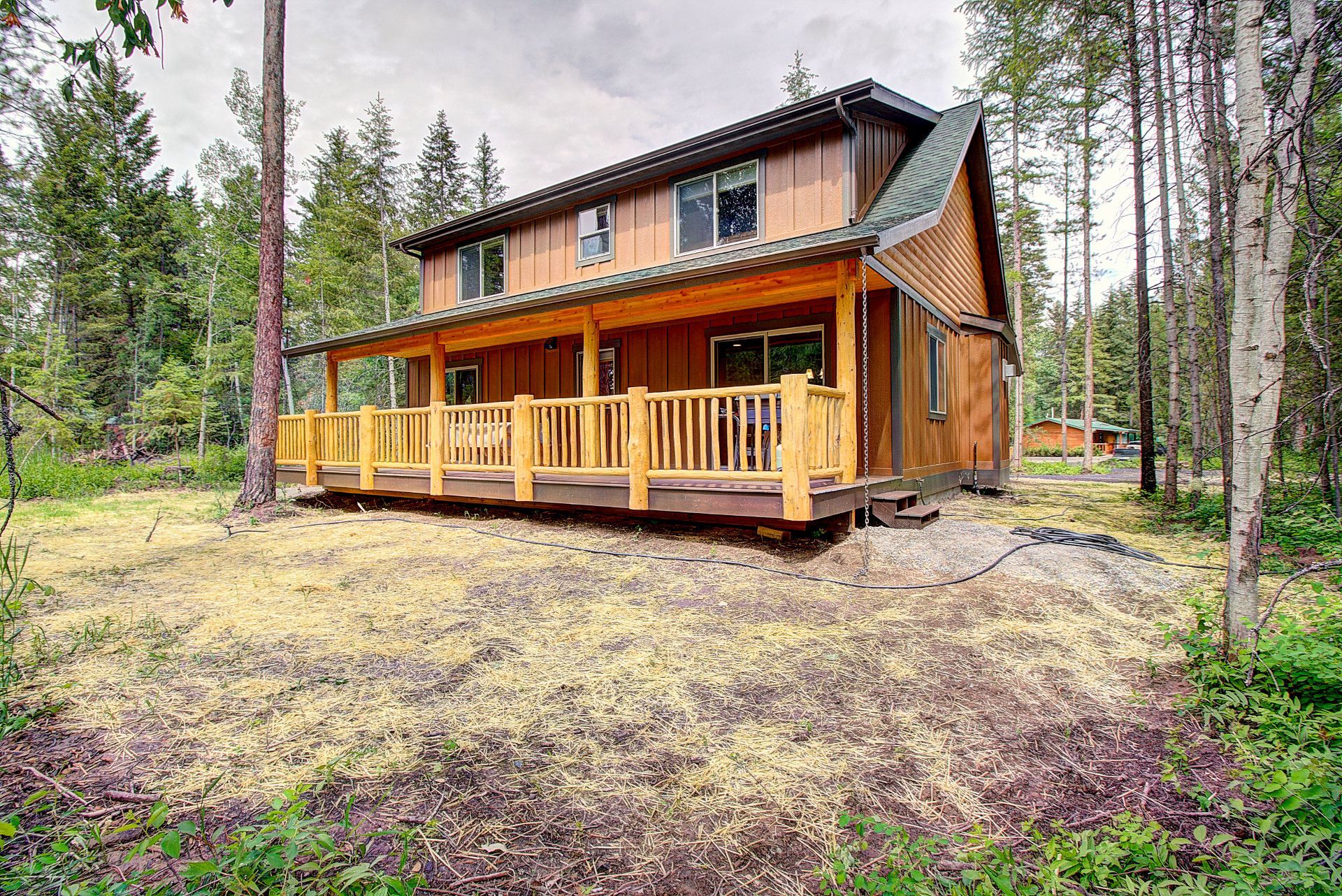 A wooden house with a large porch in the middle of a forest.