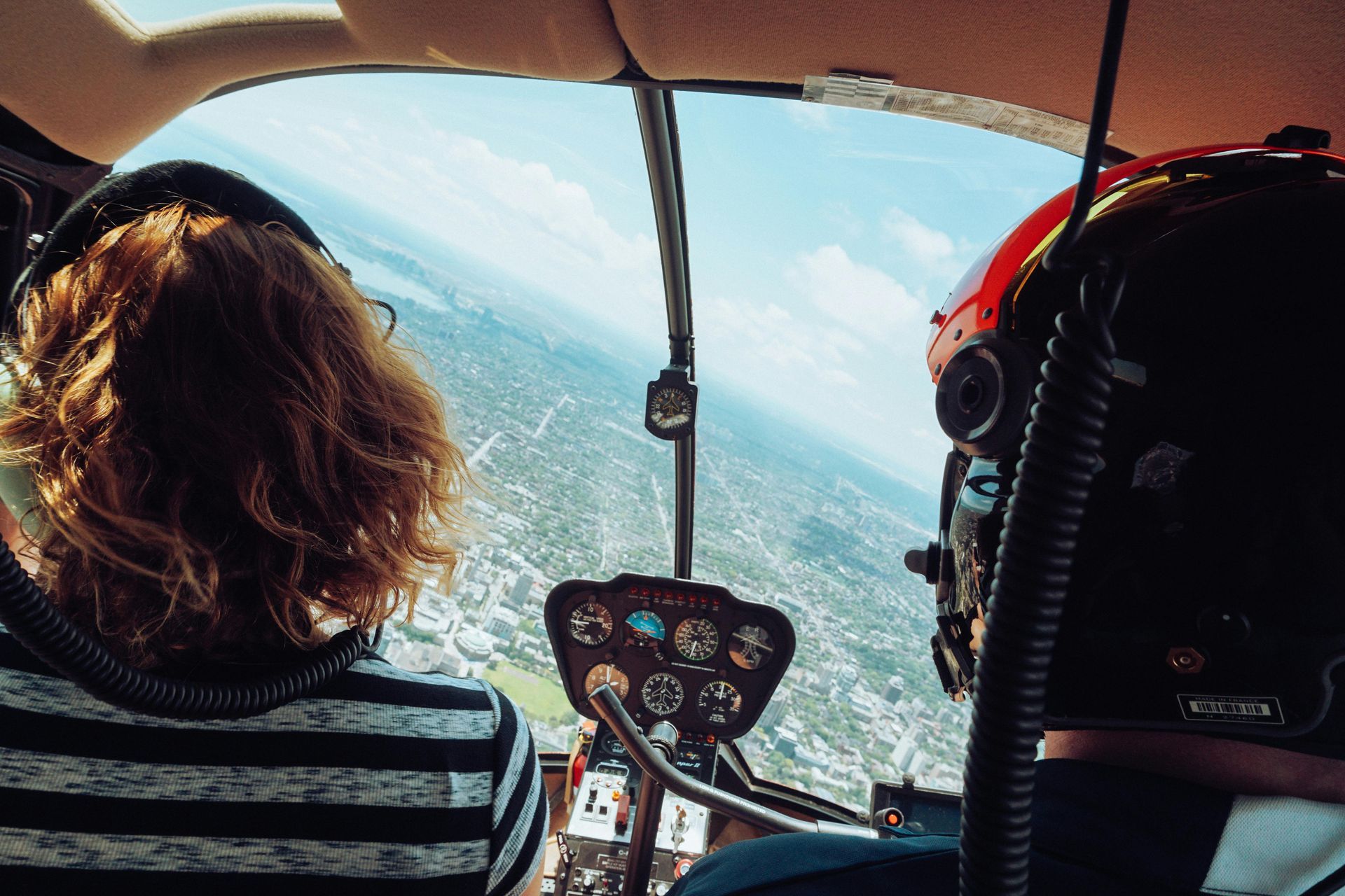 Two people are sitting in the cockpit of a helicopter looking out the window.