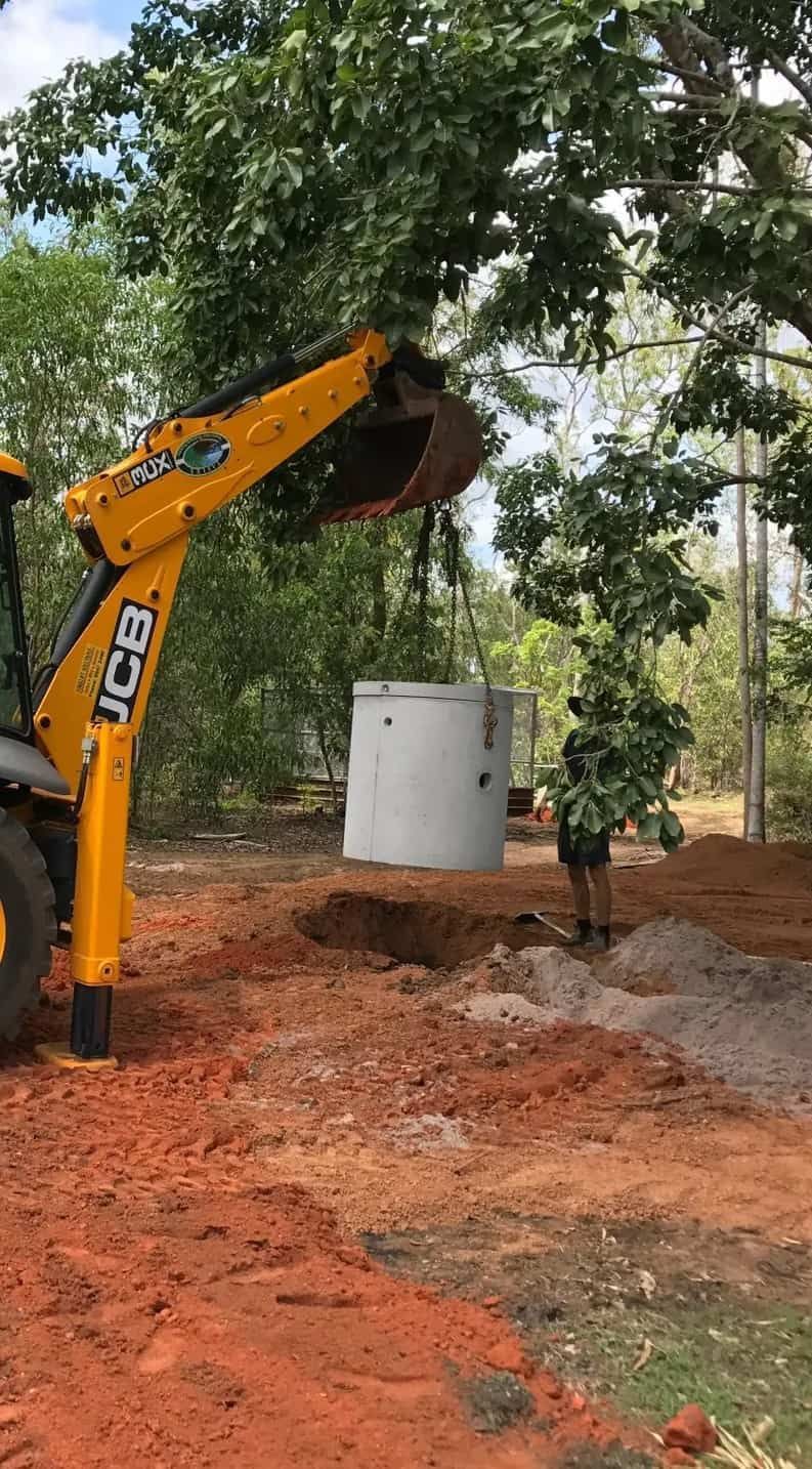 A Yellow Excavator is Lifting a Large Concrete Cylinder Into a Hole — Fastcall Group In Herbert, NT