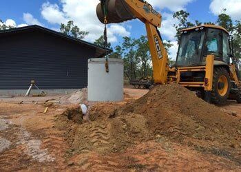 A Yellow Excavator is Digging a Hole in the Dirt in Front of a House — Fastcall Group In Herbert, NT
