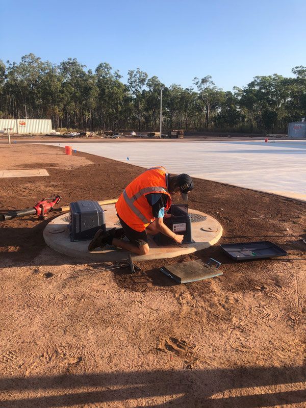 A Man in an Orange Vest is Kneeling Down in the Dirt Working on a Hole — Fastcall Group In Herbert, NT