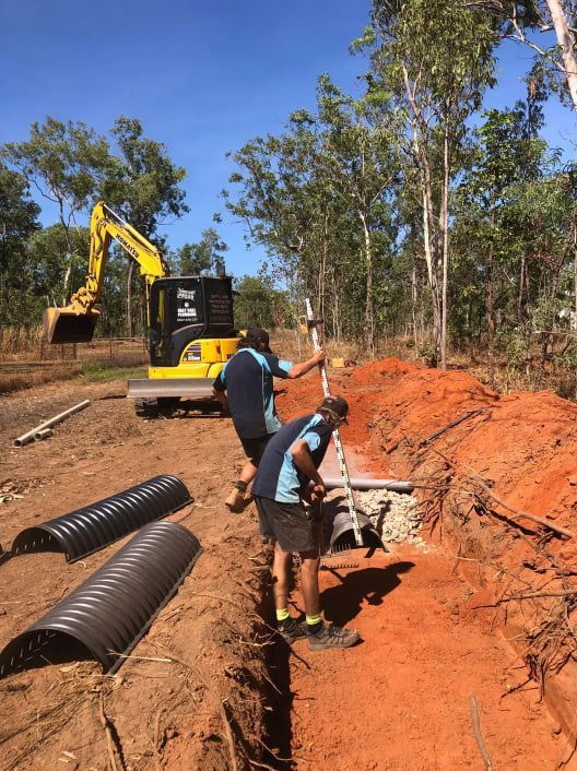 A Man is Digging a Hole in the Dirt in Front of a Yellow Excavator — Fastcall Group In Herbert, NT