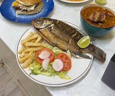 A plate of food with fish , french fries , tomatoes and radishes on a table.