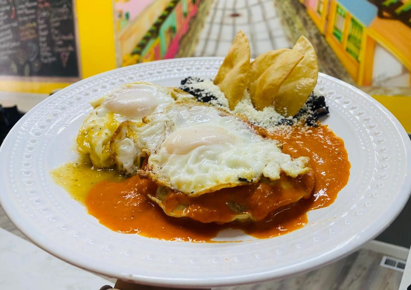A person is holding a plate of food with eggs and sauce.