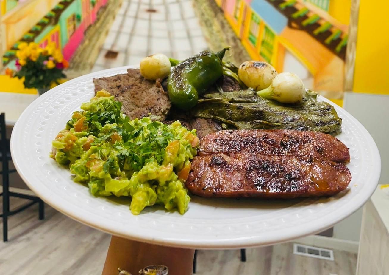 A plate of food with rice , avocado , tomatoes and limes on a table.