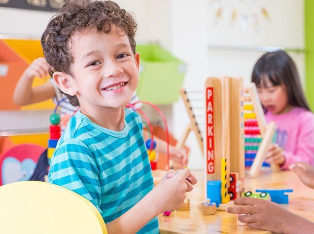 Day Care — Kindergarten students smile when playing toy in Oakland, CA