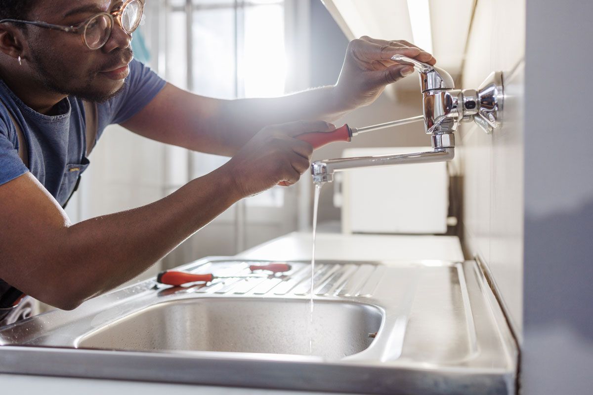 A man is fixing a faucet in a kitchen with a wrench.