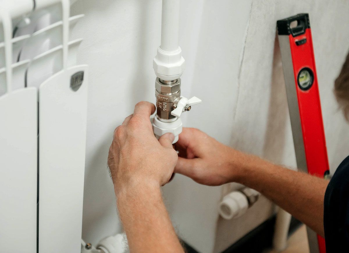 A man is fixing a pipe with a red level in the background.