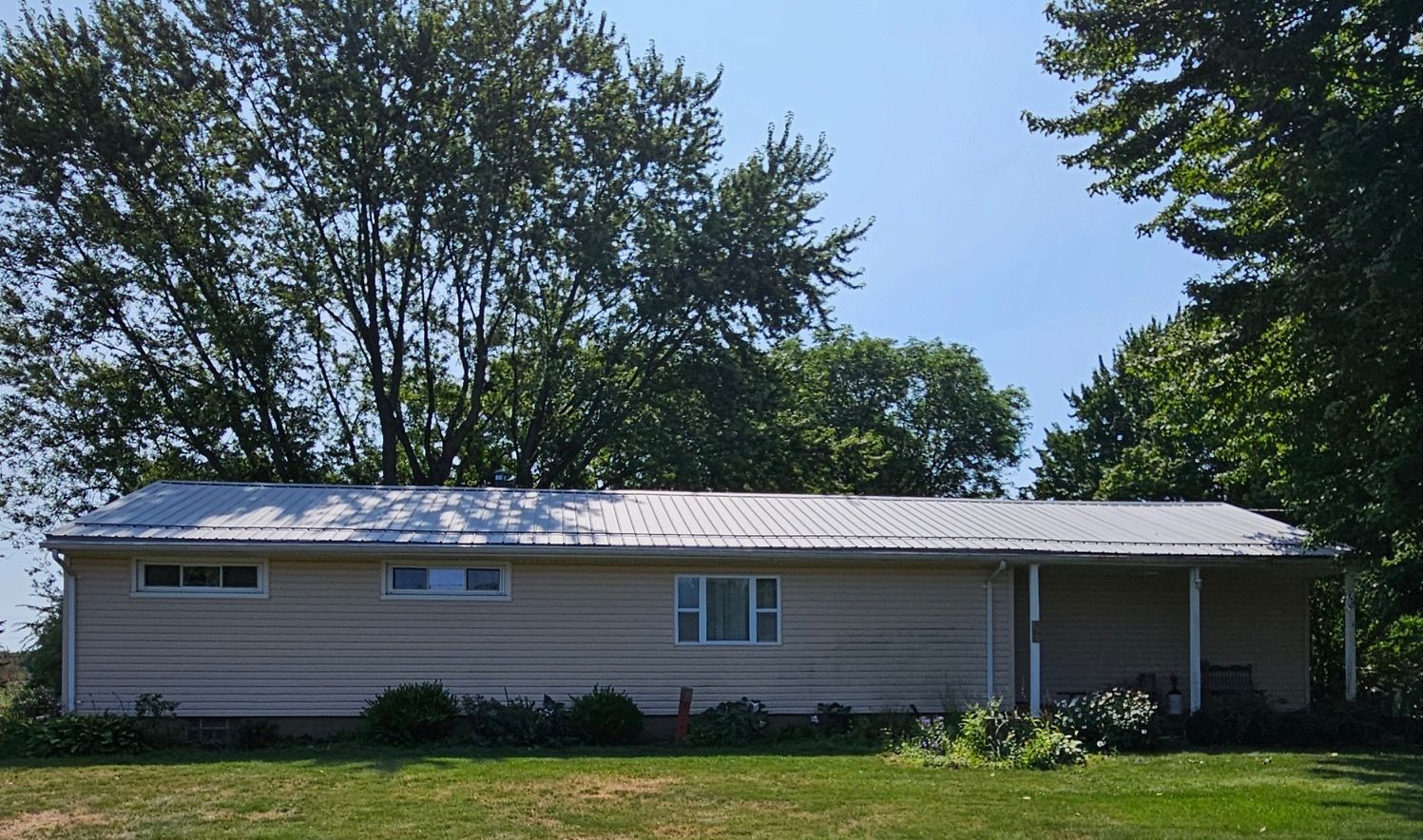 A white house with a metal roof is surrounded by trees