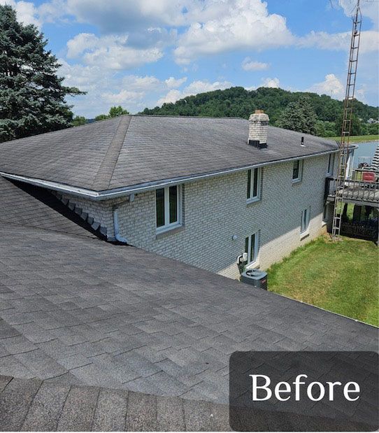 Shingled roof of a two-story brick house. Blue sky, trees in the background;