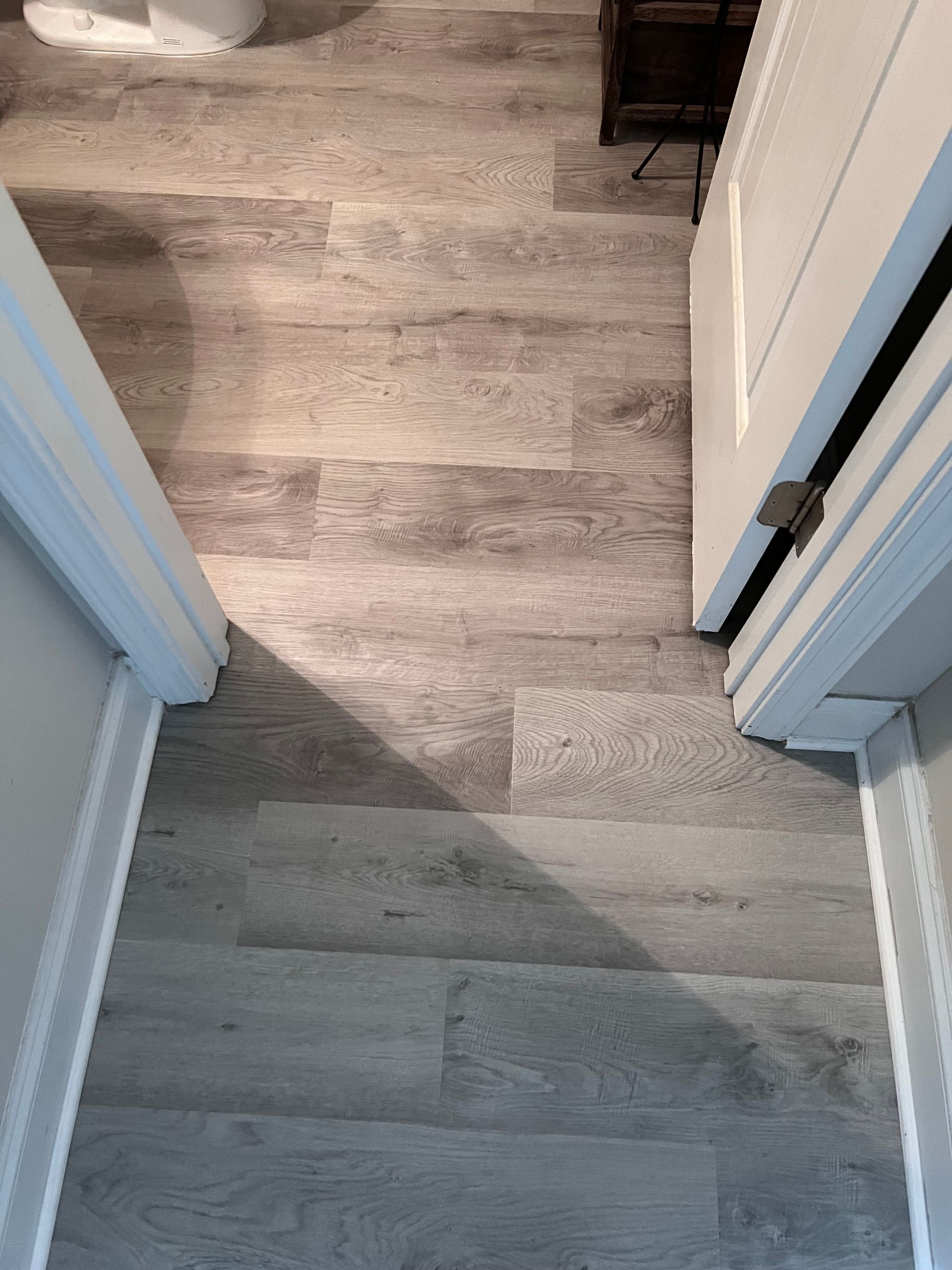 A hallway with a wooden floor and a door leading to a bathroom.