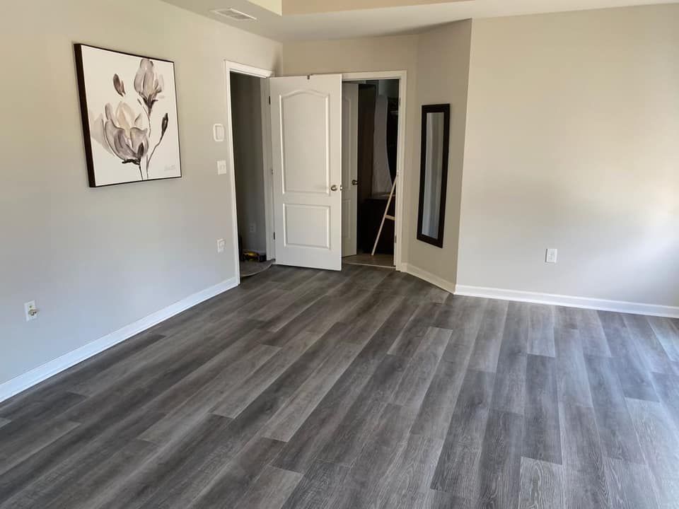 A large empty room with hardwood floors and a painting on the wall.