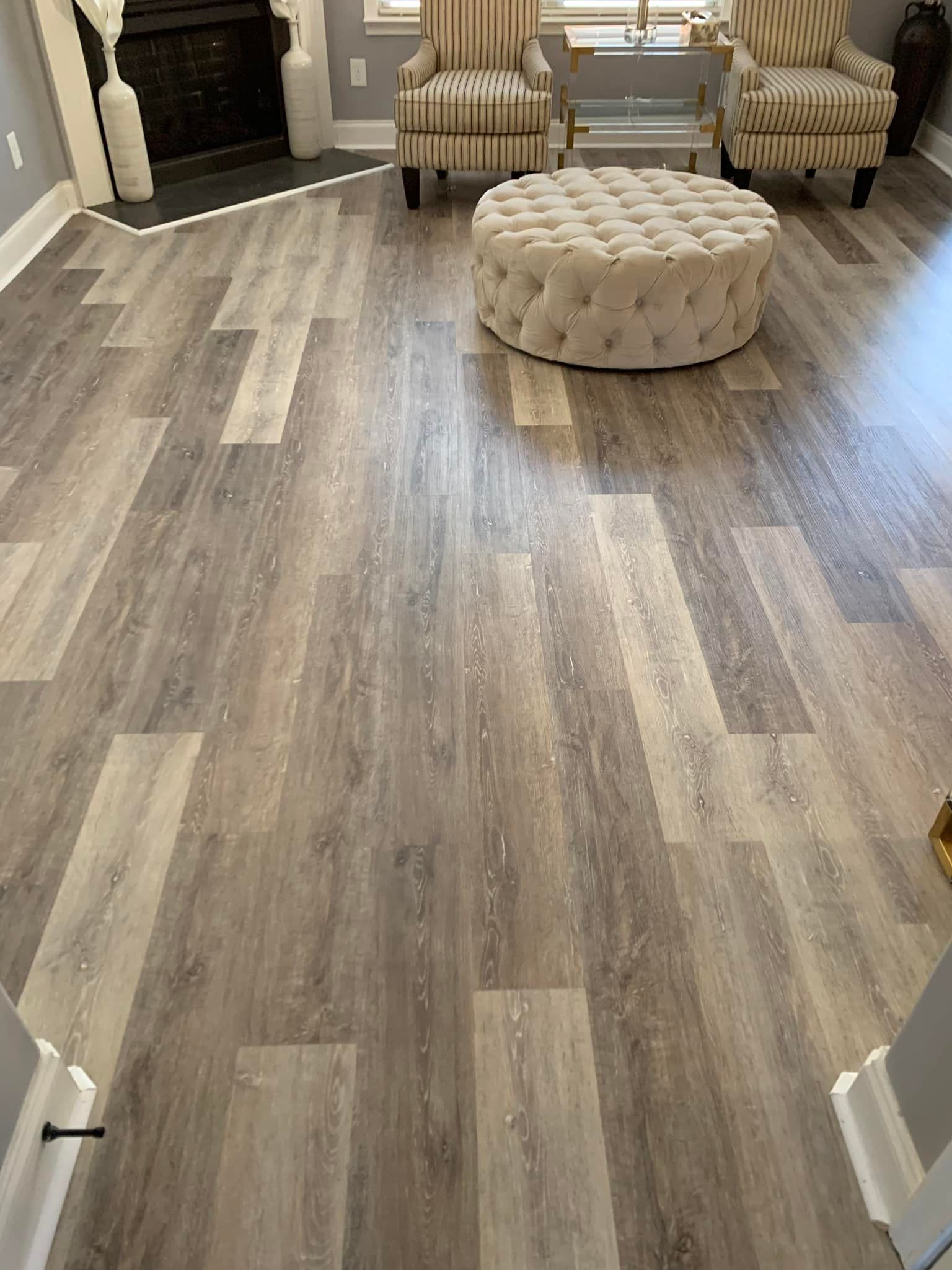 A living room with hardwood floors , two chairs and an ottoman.