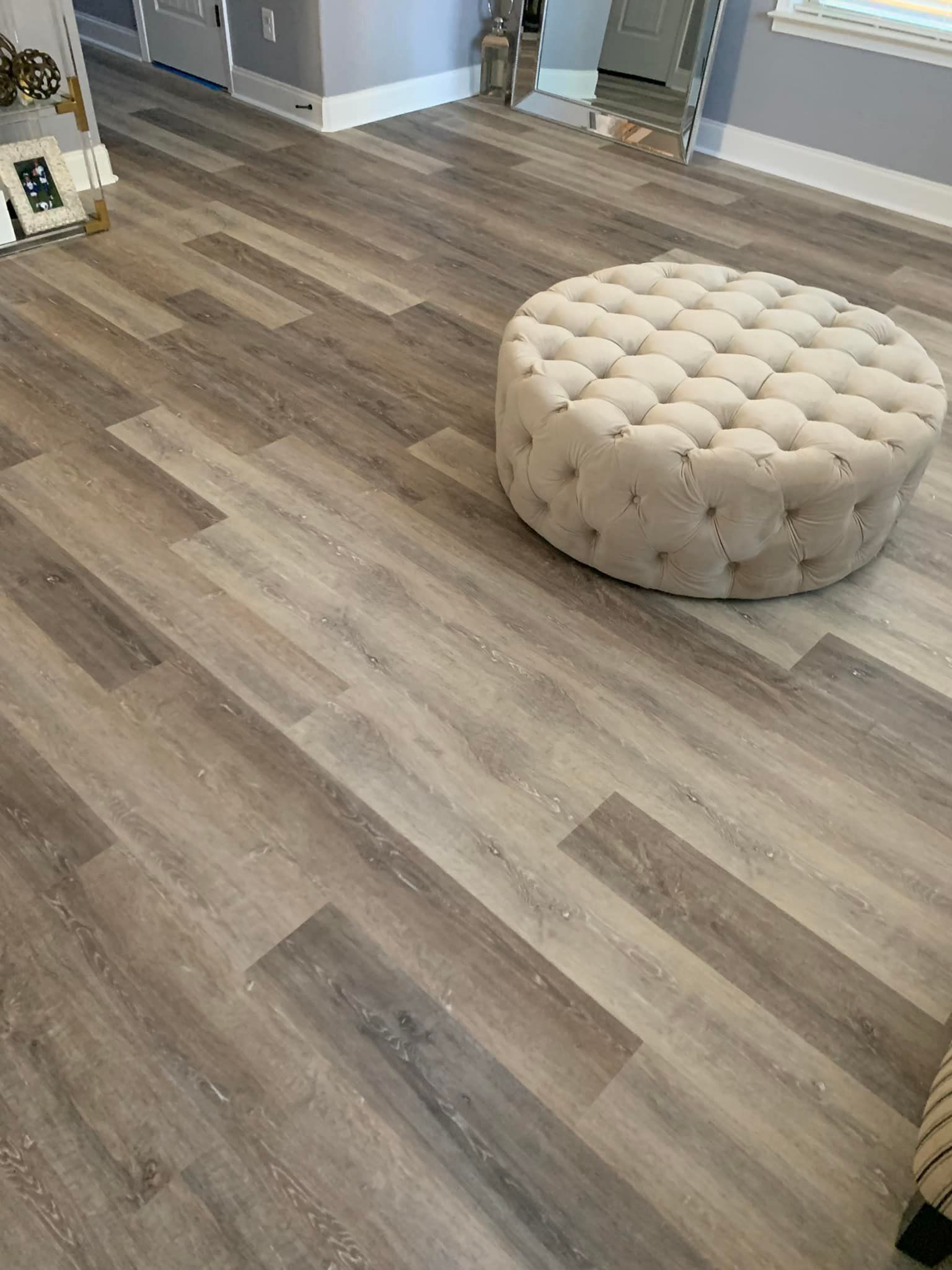 A round ottoman is sitting on a wooden floor in a living room.