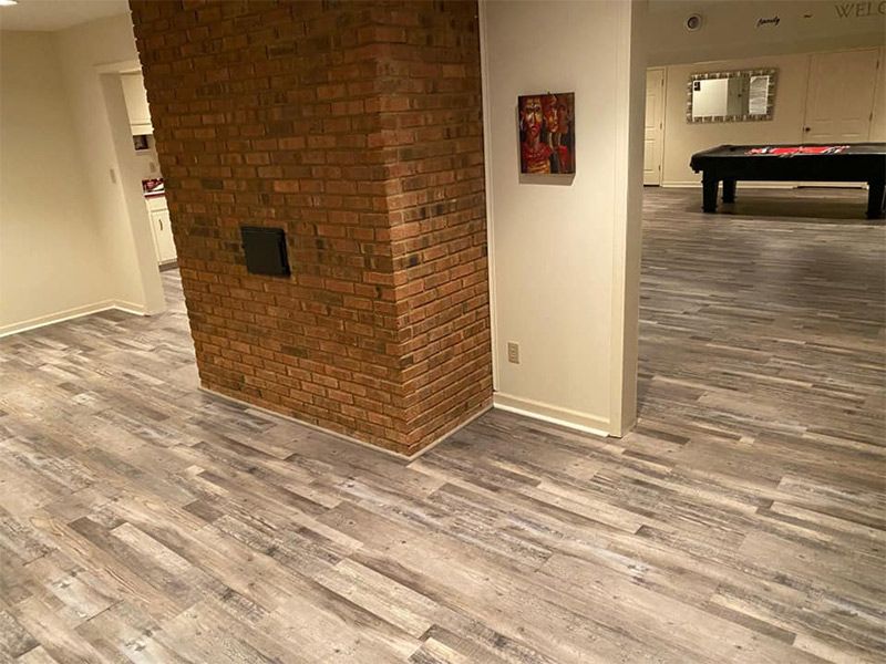 A basement with a pool table and a brick fireplace.