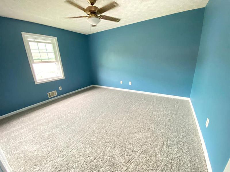 An empty bedroom with blue walls and a ceiling fan.