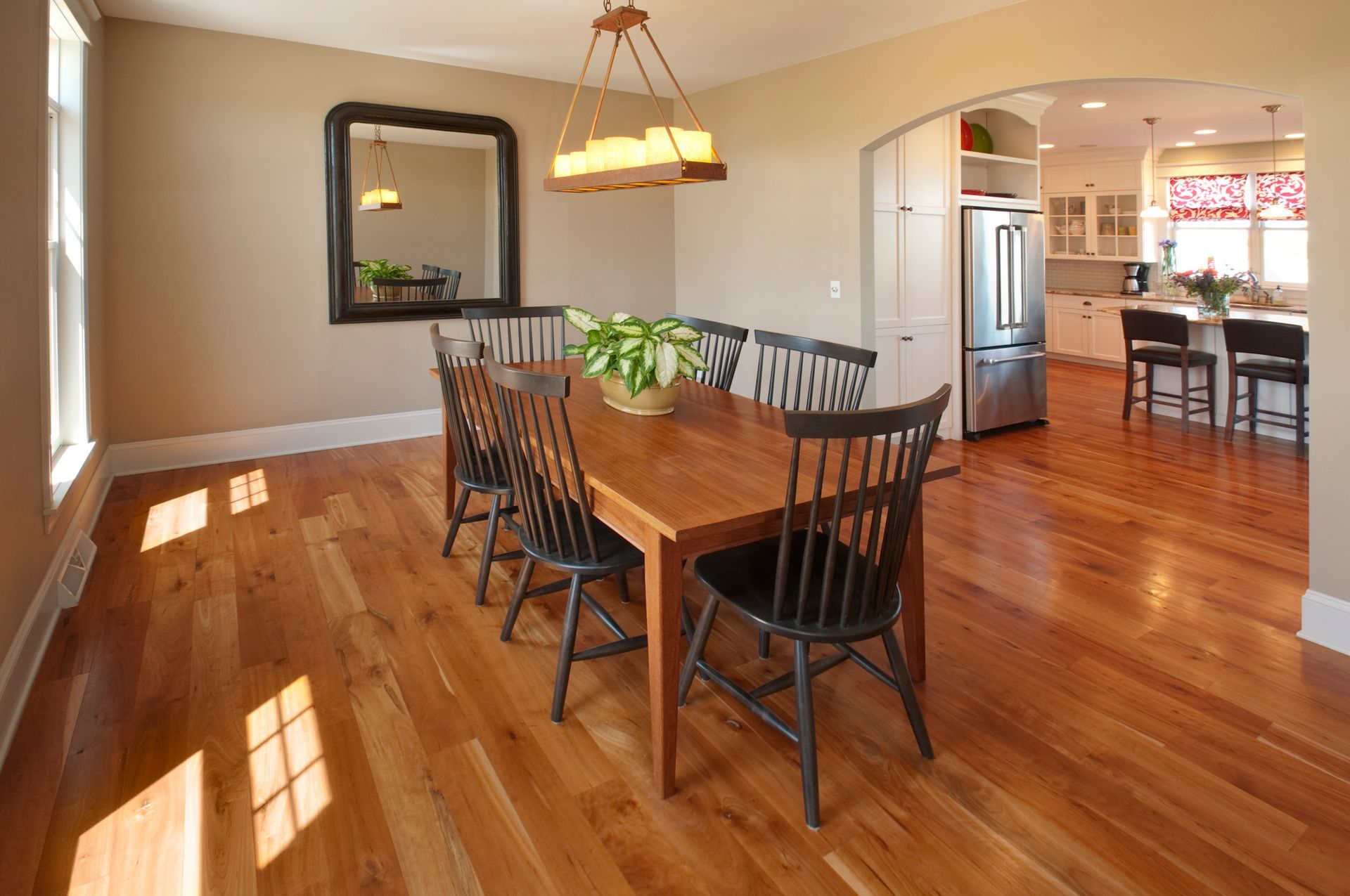 Dining room with wooden table, chairs, and hardwood floors, open to a kitchen.