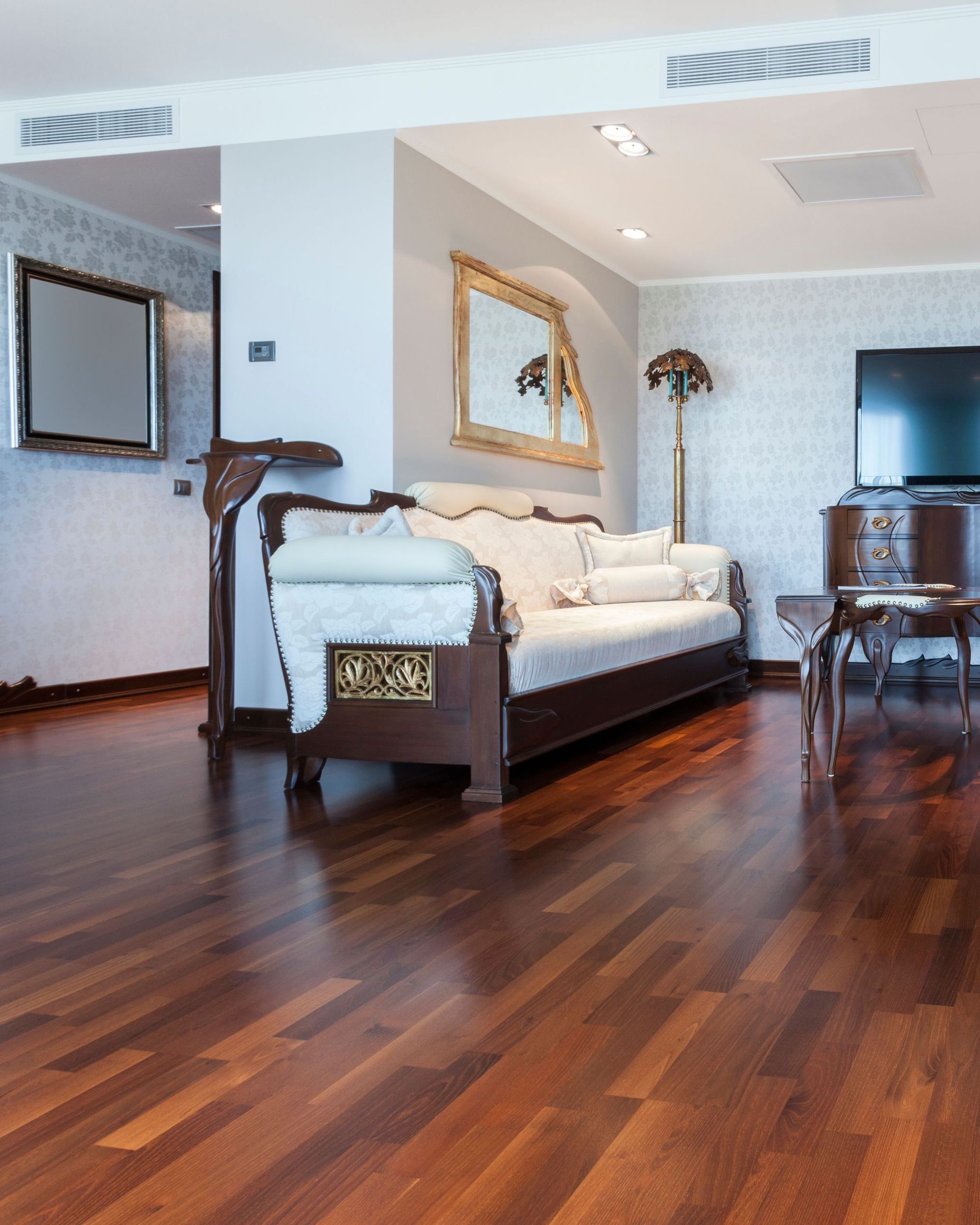 Dark hardwood floor in a living room with a sofa, ornate furniture, a TV, and a gilded mirror.