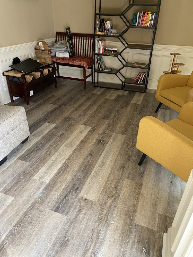 A living room with hardwood floors , chairs , a bench and a bookshelf.