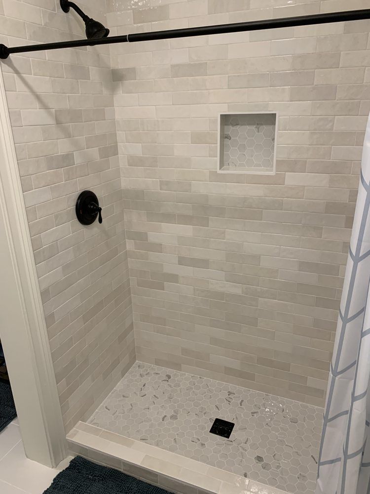 A bathroom with a walk in shower with white tiles and a black shower head.