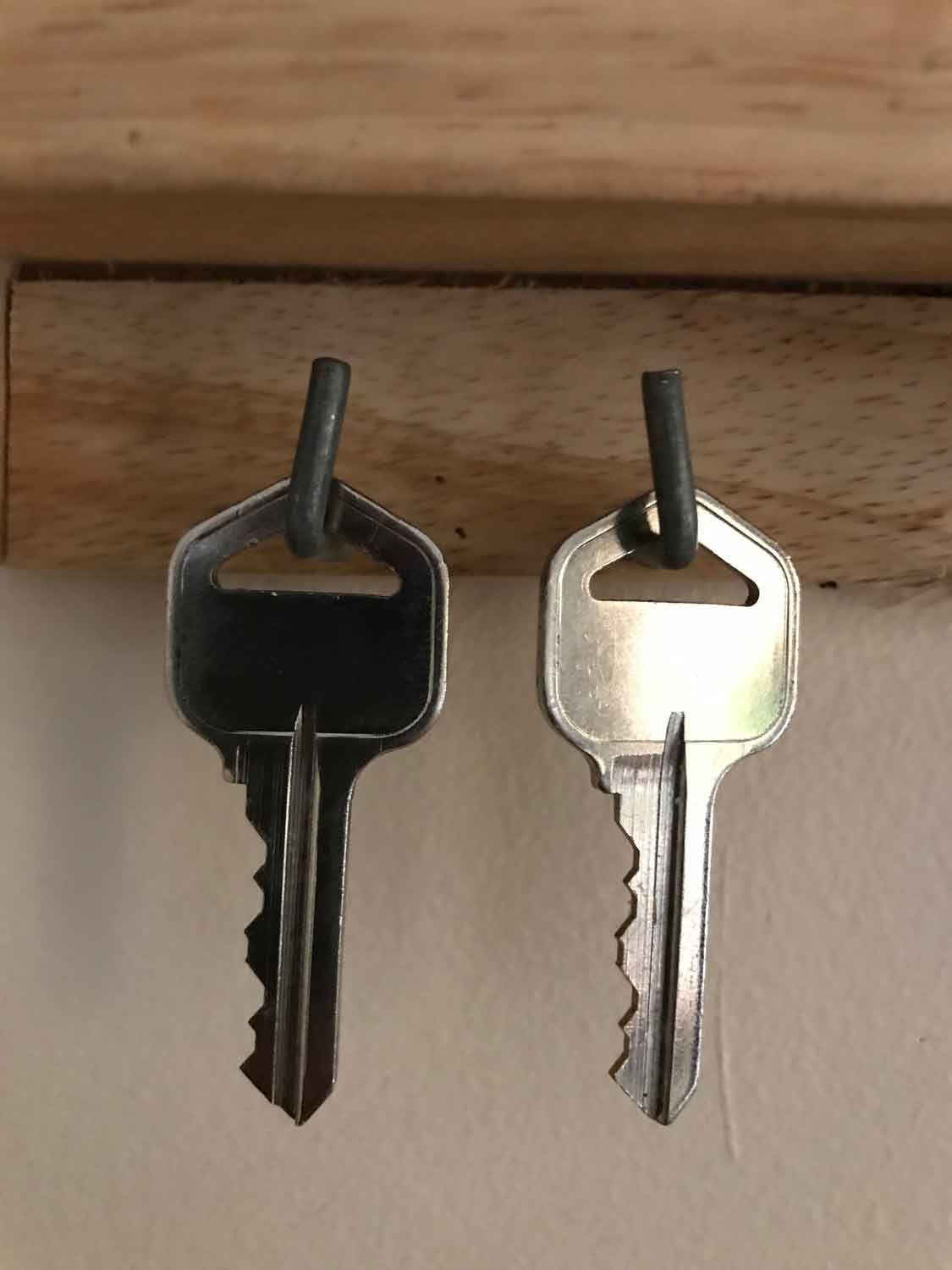 Two keys are hanging on a wooden shelf.