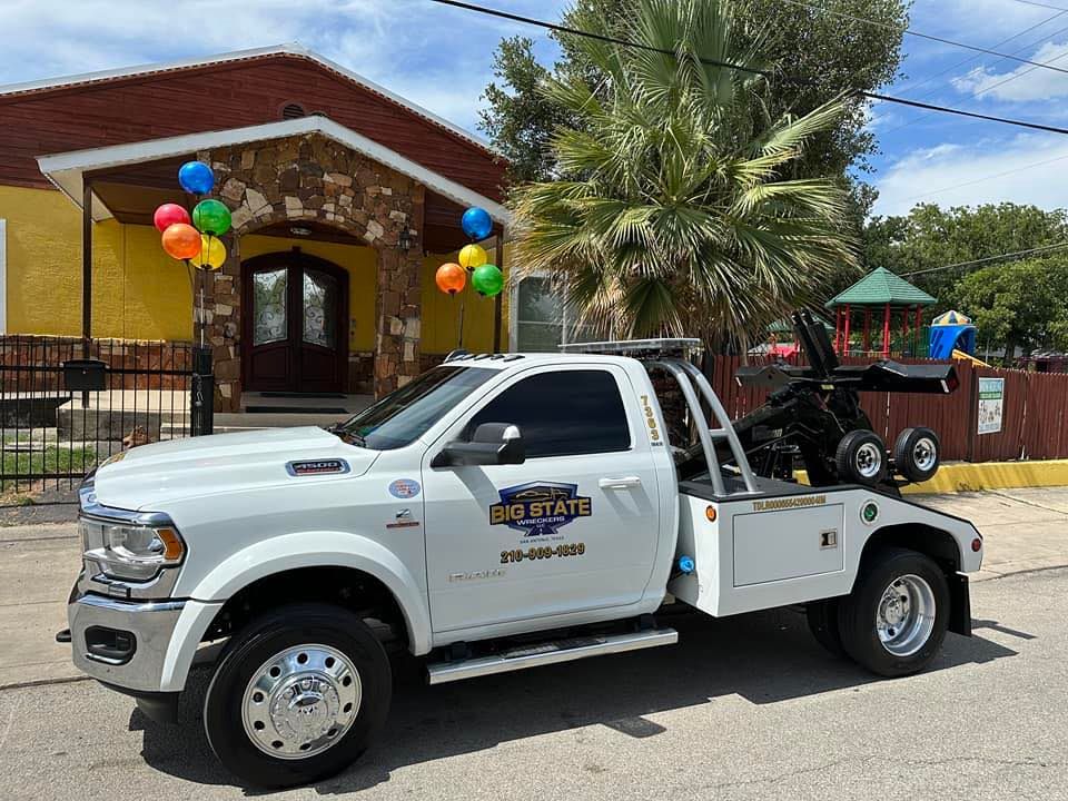 A white tow truck with a company logo parked in front of a yellow building adorned with colorful balloons.