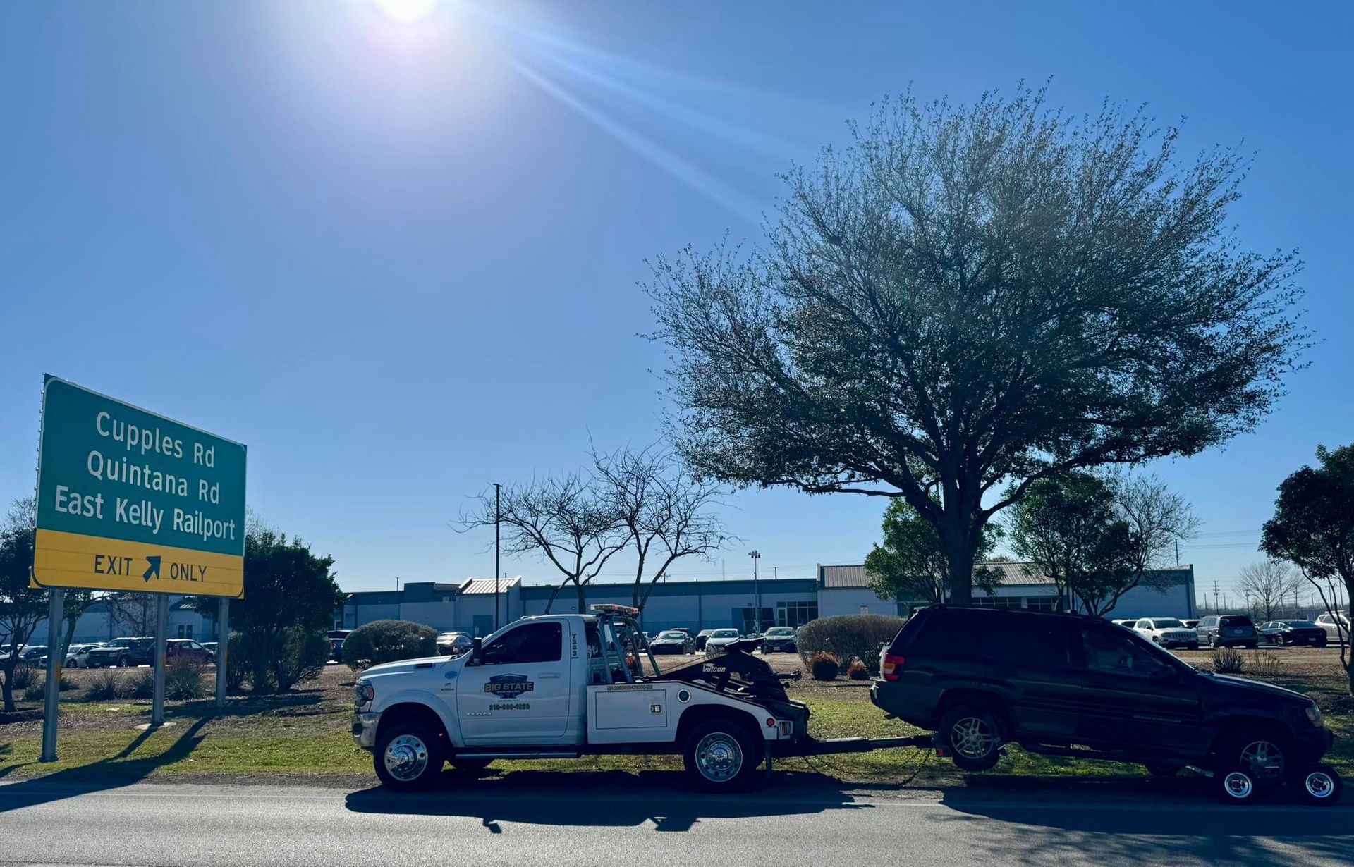 A white tow truck pulls a dark SUV on a bright, sunny day next to a highway exit sign for Gwinnett Rd and East Ridge Rd.