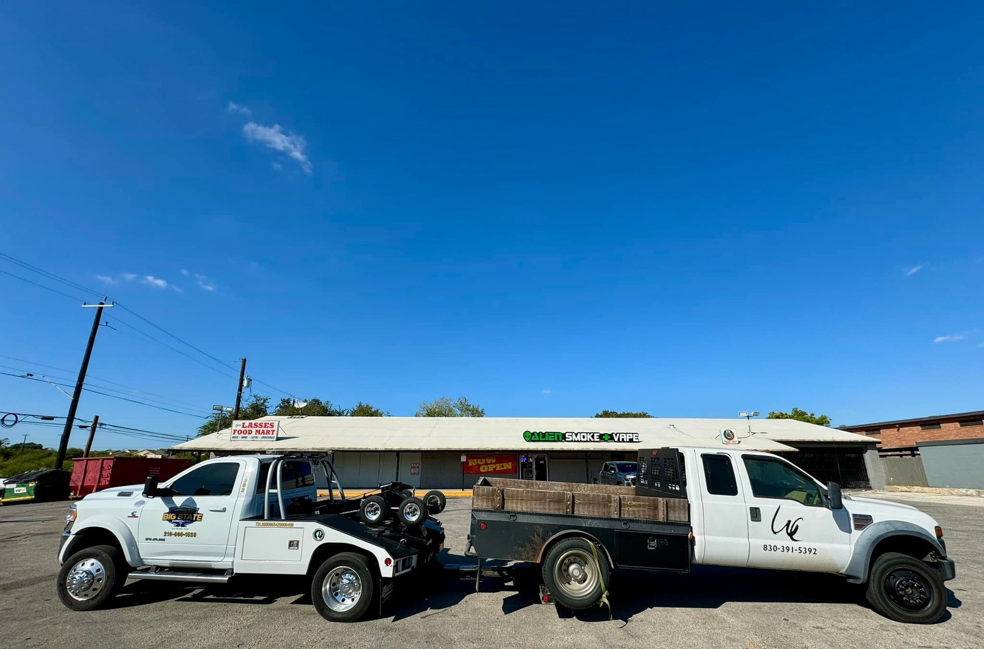 Two white work trucks parked in a gravel lot in front of a commercial building under a clear blue sky.