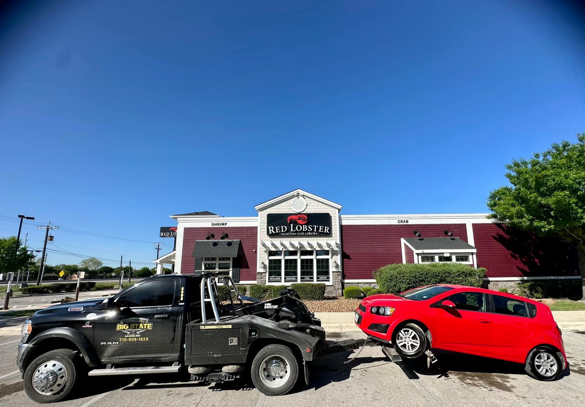 A black tow truck towing a red car in front of a building with a red exterior under a clear blue sky.